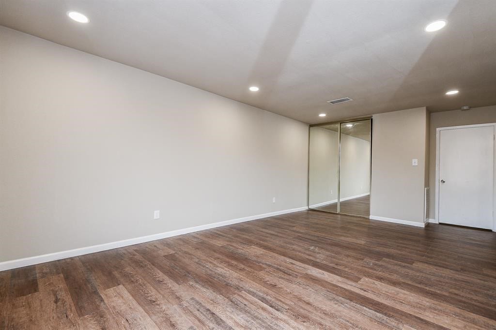 12569 Wellington Park Drive, Houston, TX 77072 This room features a spacious layout with wood-style flooring, recessed lighting, and neutral walls. It includes a mirrored sliding closet door and a white door, offering a modern and clean look.