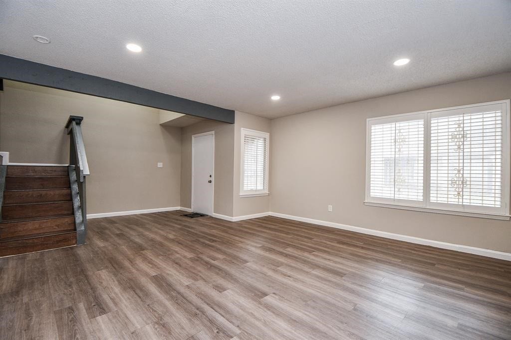 12569 Wellington Park Drive, Houston, TX 77072 This spacious living area features modern laminate flooring, neutral walls, recessed lighting, and large windows with blinds. The dark wood staircase adds character, leading to the upper level, and there's a convenient side door for easy access.