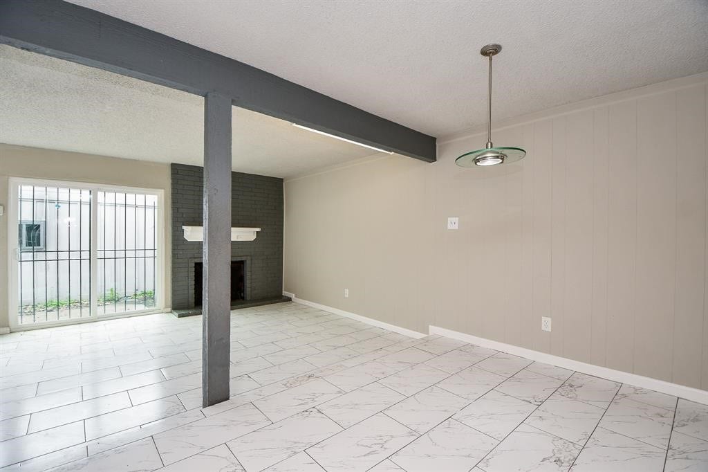 12569 Wellington Park Drive, Houston, TX 77072 This room features a spacious open layout with light tile flooring and neutral walls. It includes a cozy brick fireplace, sliding glass doors leading outside, and a modern ceiling light fixture. Ideal for a living or dining area.