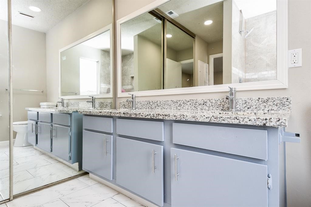 12569 Wellington Park Drive, Houston, TX 77072 This bathroom features a dual-sink vanity with granite countertops, large mirrors, and light blue cabinetry. The space includes modern fixtures and a neutral color palette, complemented by a tiled floor and shower area.