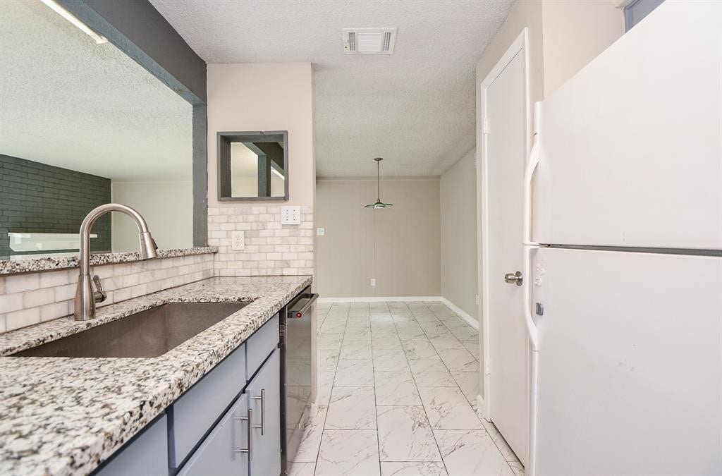 12569 Wellington Park Drive, Houston, TX 77072 This photo showcases a modern kitchen with granite countertops, a large sink, and sleek cabinetry. It opens into a dining area with tiled flooring and neutral walls, offering a bright and open feel.