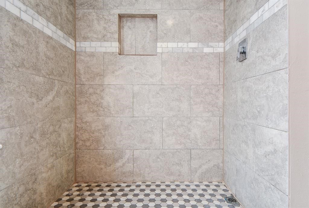 12569 Wellington Park Drive, Houston, TX 77072 Spacious shower with elegant stone tiles, featuring a built-in niche and stylish hexagonal floor tiles. Perfect for a modern bathroom.