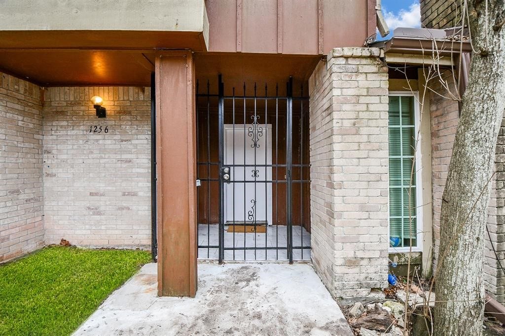 12569 Wellington Park Drive, Houston, TX 77072 This photo shows the entrance of a home with a gated entryway. It features brick walls, a small grassy area to the left, and a window to the right. A light fixture is mounted above the house number.