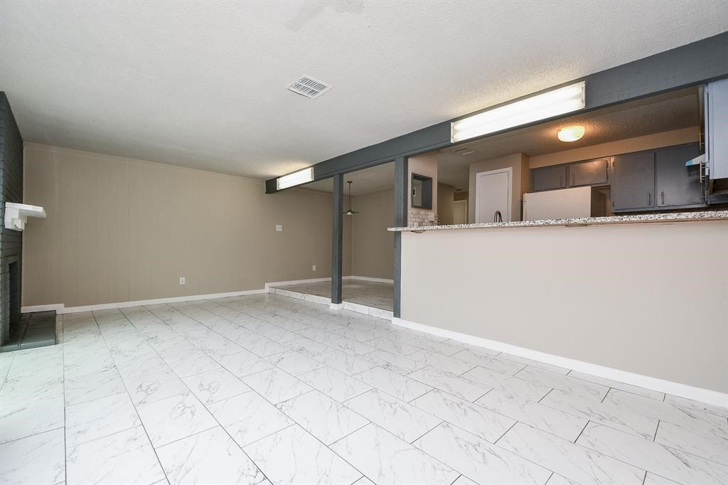 12569 Wellington Park Drive, Houston, TX 77072 Spacious living area with modern tiled flooring, open layout, and a raised kitchen bar. The room features neutral tones and a cozy fireplace, creating an inviting atmosphere.