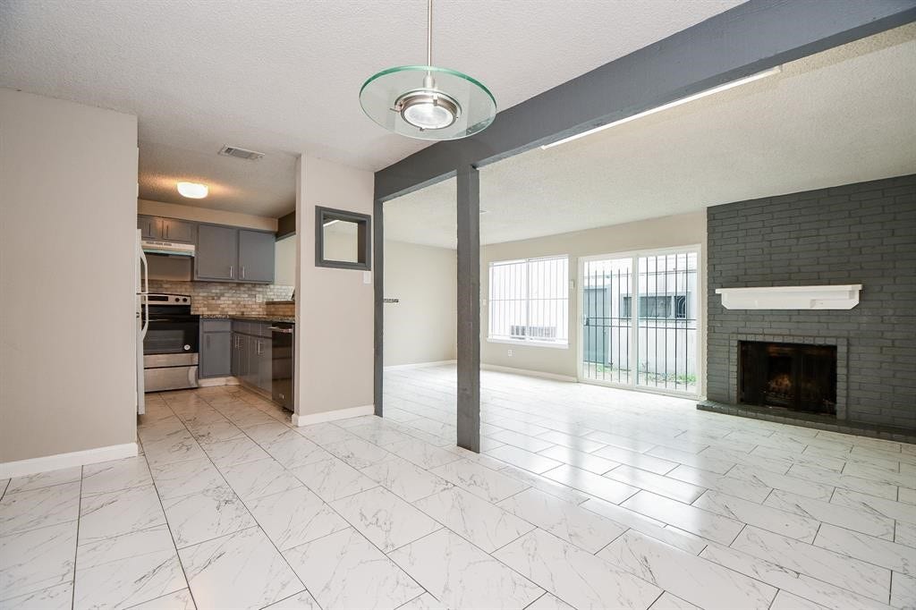 12569 Wellington Park Drive, Houston, TX 77072 This photo showcases a bright, open-concept living area featuring large windows, a modern kitchen with stainless steel appliances, and a cozy fireplace. The space has sleek tile flooring and a contemporary design, perfect for comfortable living and entertaining.