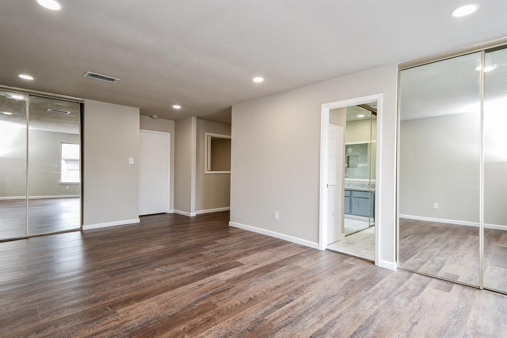 12569 Wellington Park Drive, Houston, TX 77072 Spacious room with hardwood flooring, neutral walls, and recessed lighting. Features mirrored sliding closet doors and an attached bathroom, creating a modern, open feel.