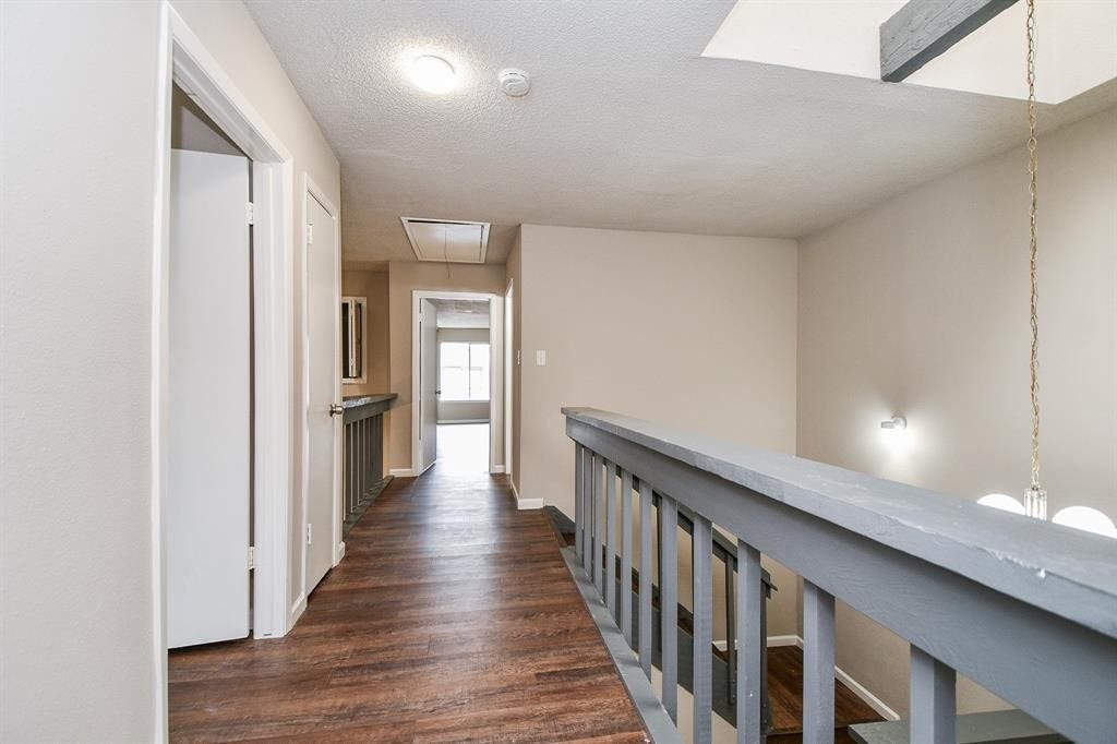 12569 Wellington Park Drive, Houston, TX 77072 This photo shows a hallway with wood flooring, neutral walls, and a staircase railing. It leads to a bright room with a window at the end, offering a clean and open feel.