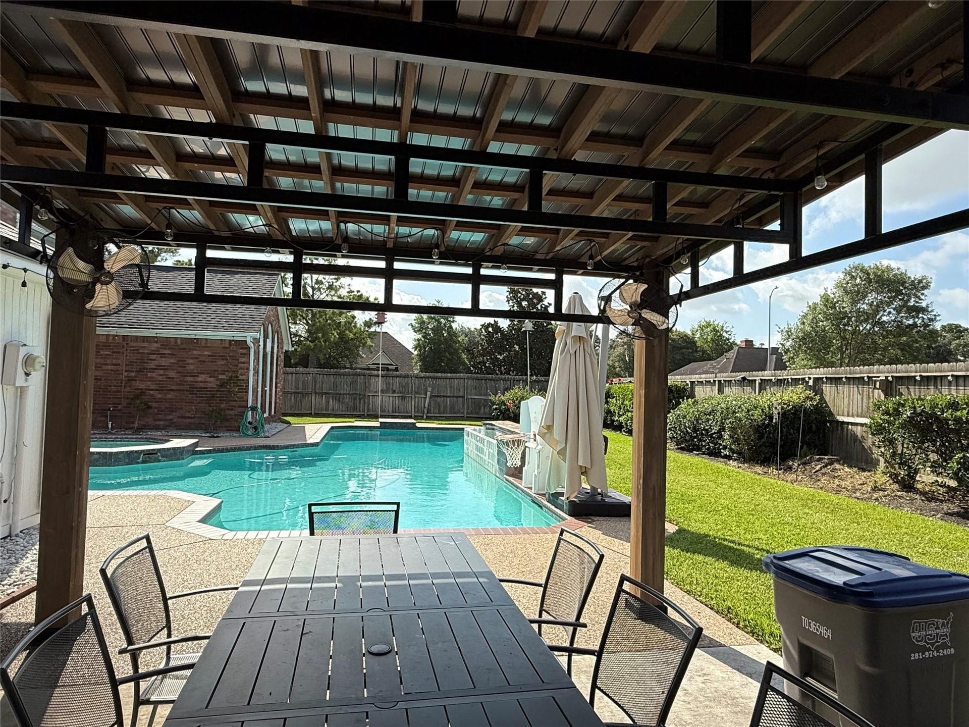The inviting covered patio offers a serene view of the sparkling pool and lush green space, perfect for relaxation and entertainment.