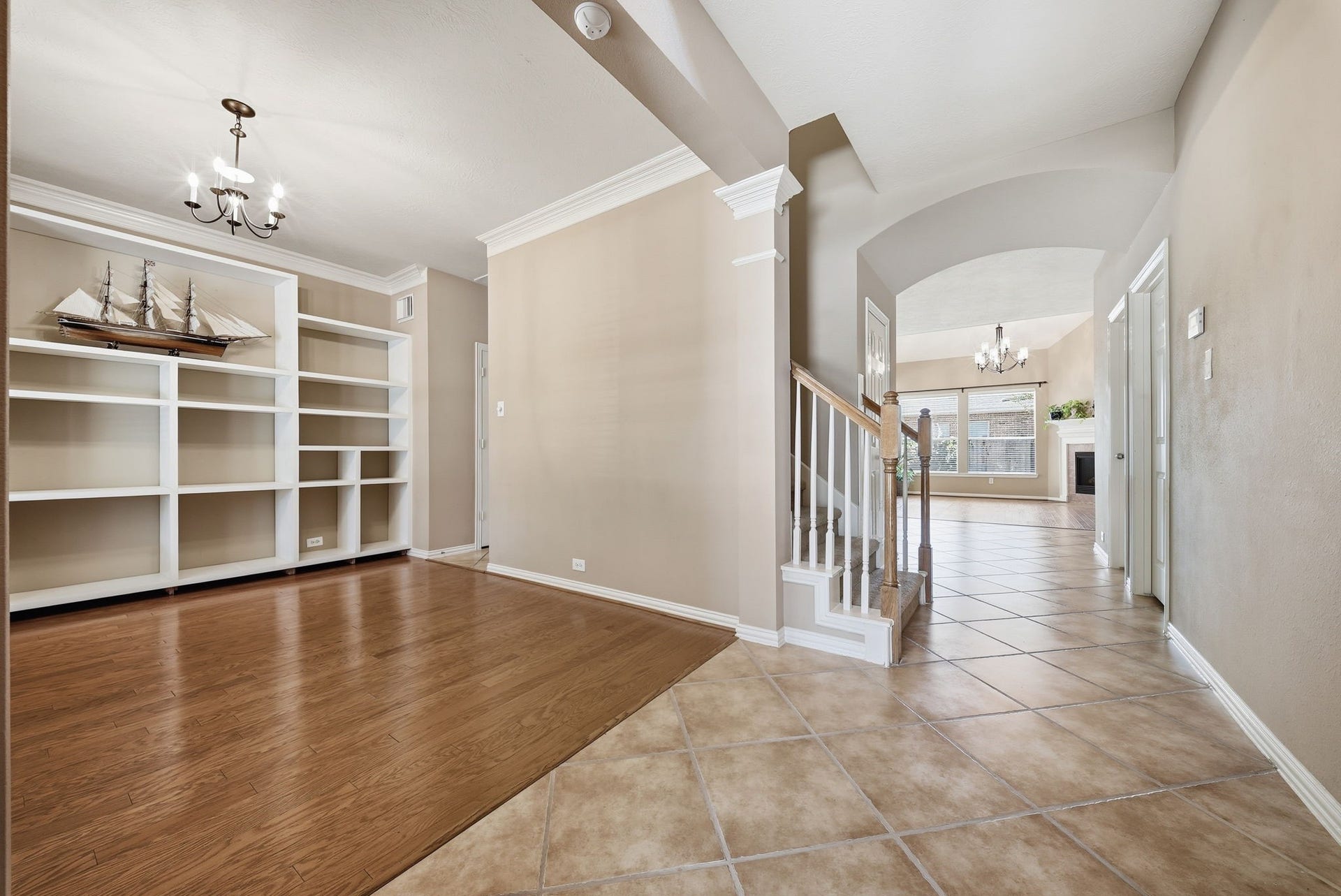 The formal dining area features built-in shelving and office flexibility, with the hallway to the left leading to the kitchen. An arched foyer beside the wood-railed staircase opens to the bright living room.