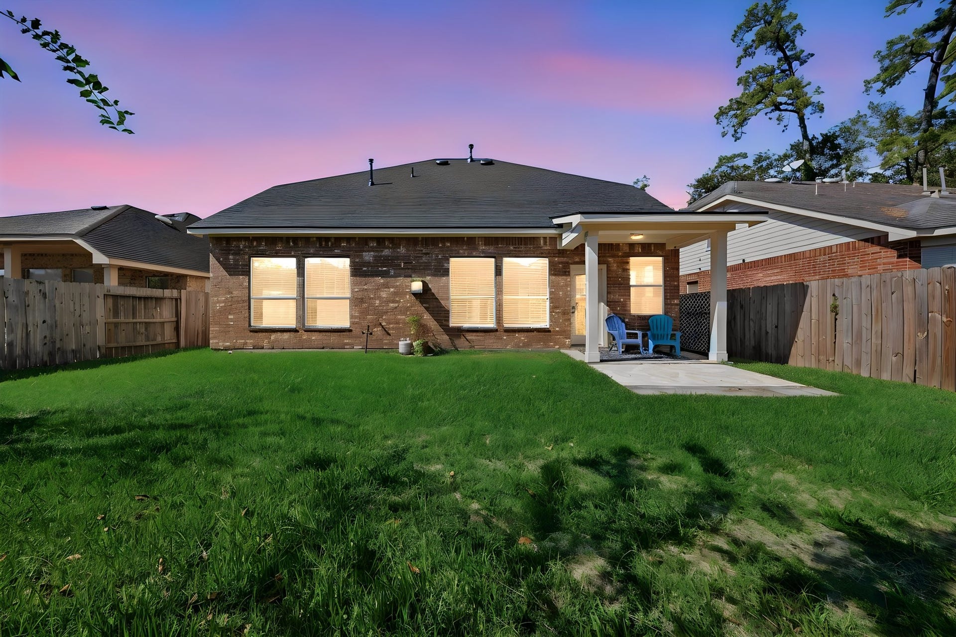*TWILIGHT VIEW* Spacious fenced backyard offers room to play, garden, or entertain, with a covered patio and extended concrete area for outdoor seating and grilling.
