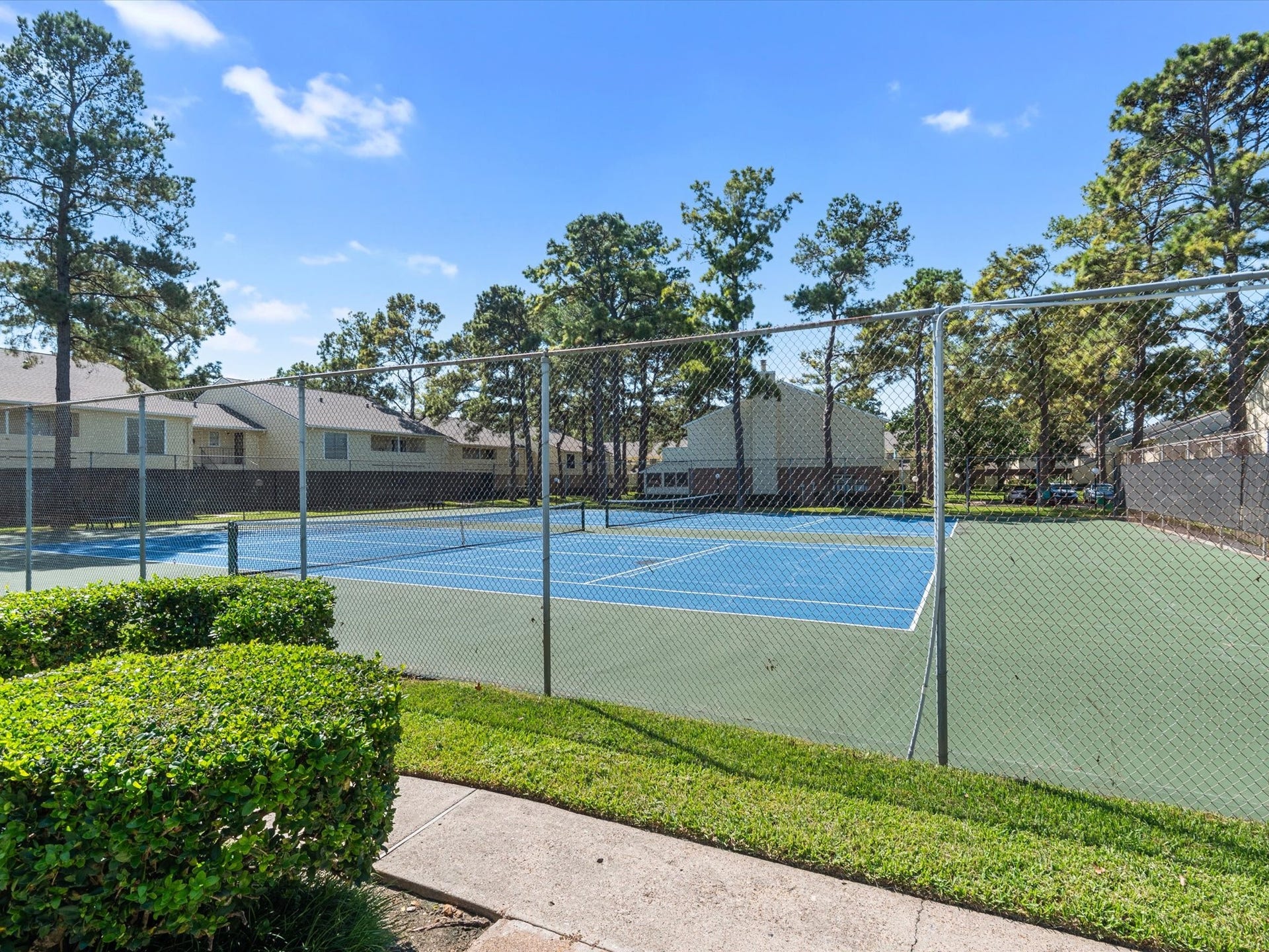 Community tennis courts surrounded by mature trees and greenery.