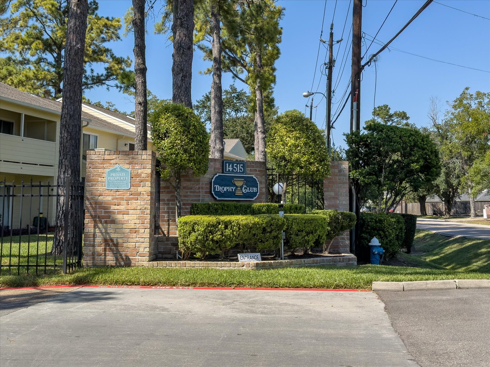 Welcoming entrance to the condo community, surrounded by mature trees and landscaping.