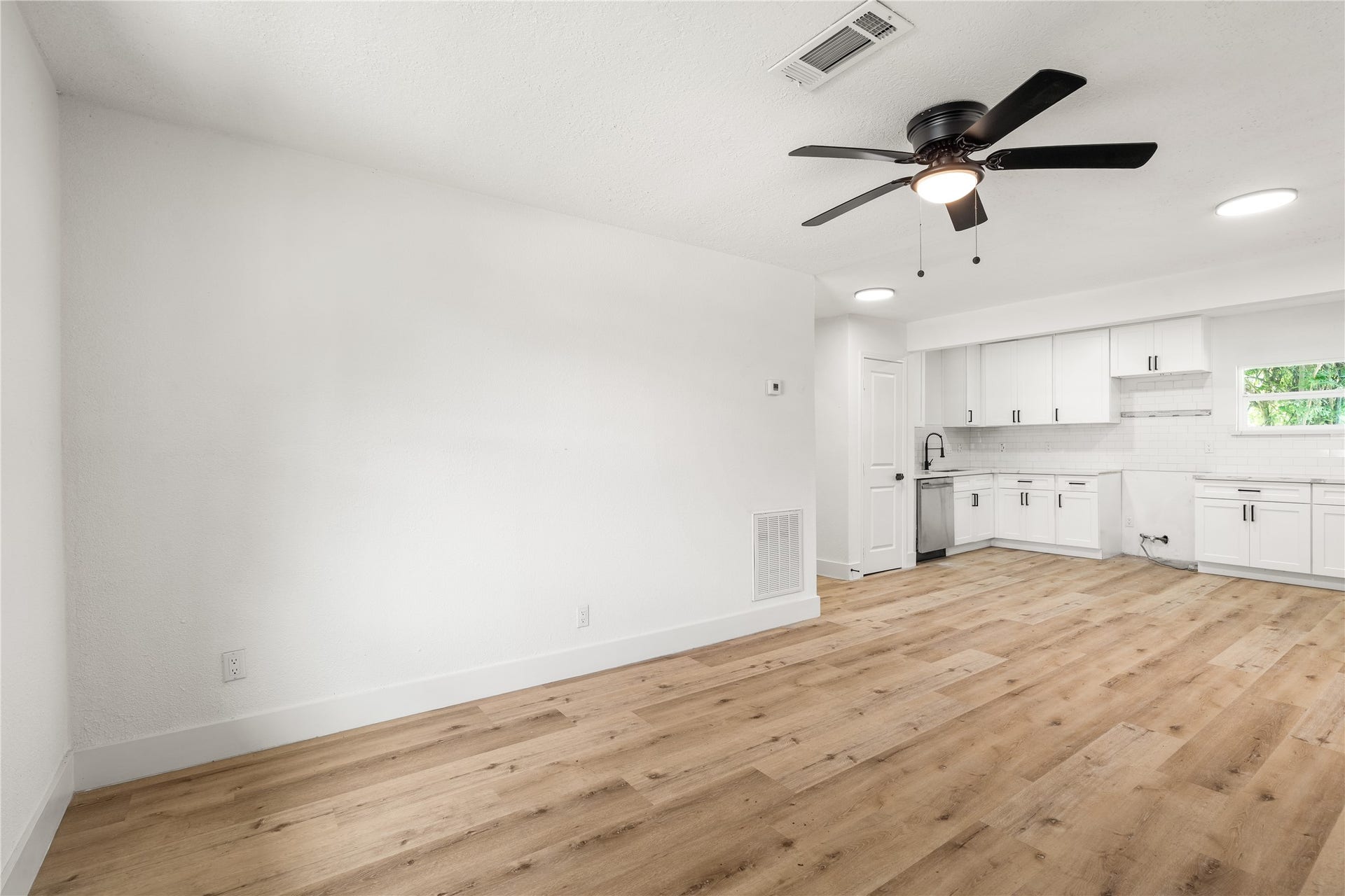 3048 Briarwick Lane, Houston, TX 77093 Wide-angle view taken from the main living room wall, showing side window light, warm wood-grain floors, and an open layout looking directly into the kitchen.