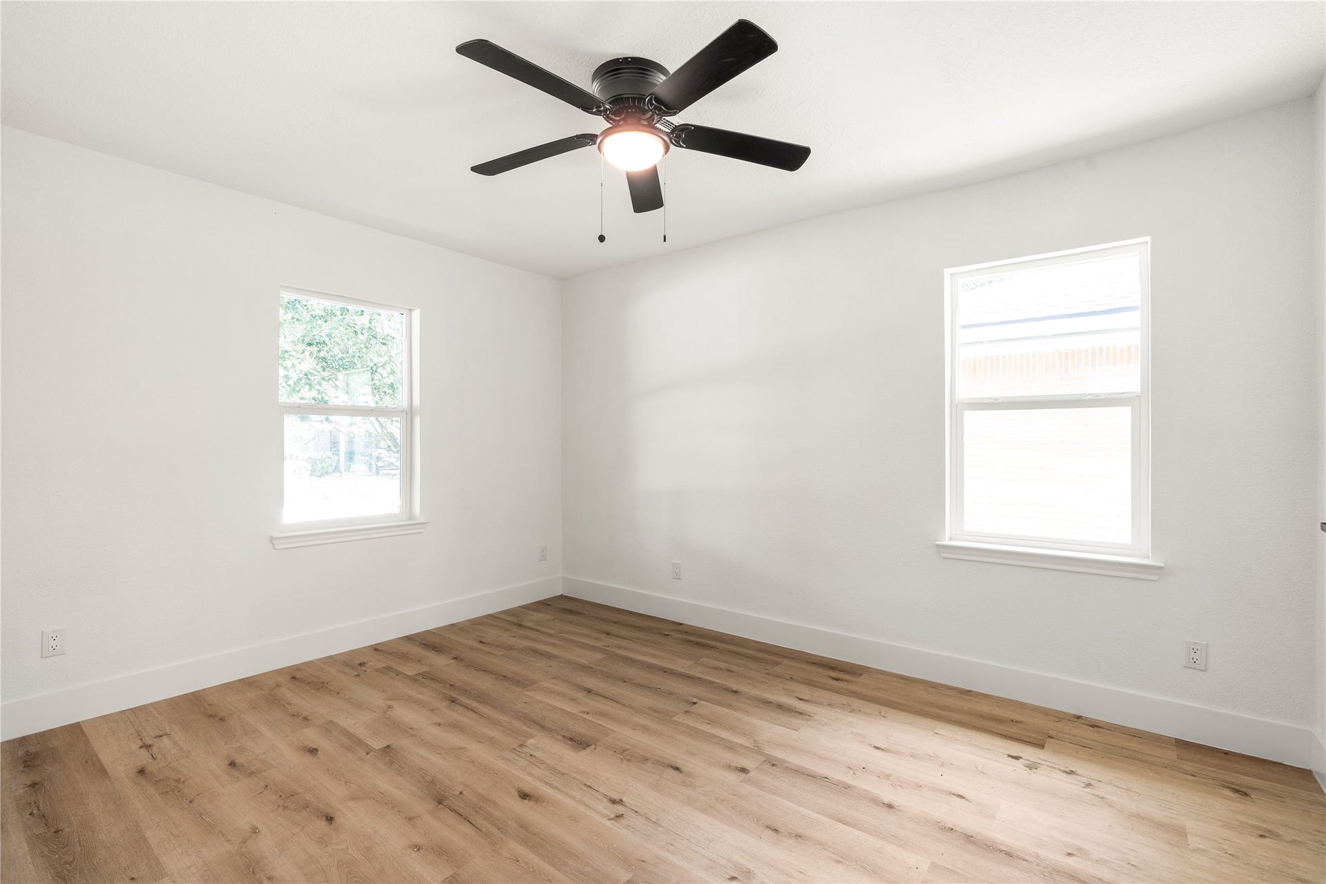 3048 Briarwick Lane, Houston, TX 77093 Bright bedroom corner featuring dual windows, modern ceiling fan, and warm wood-grain flooring. Ideal for a guest room or quiet home office.