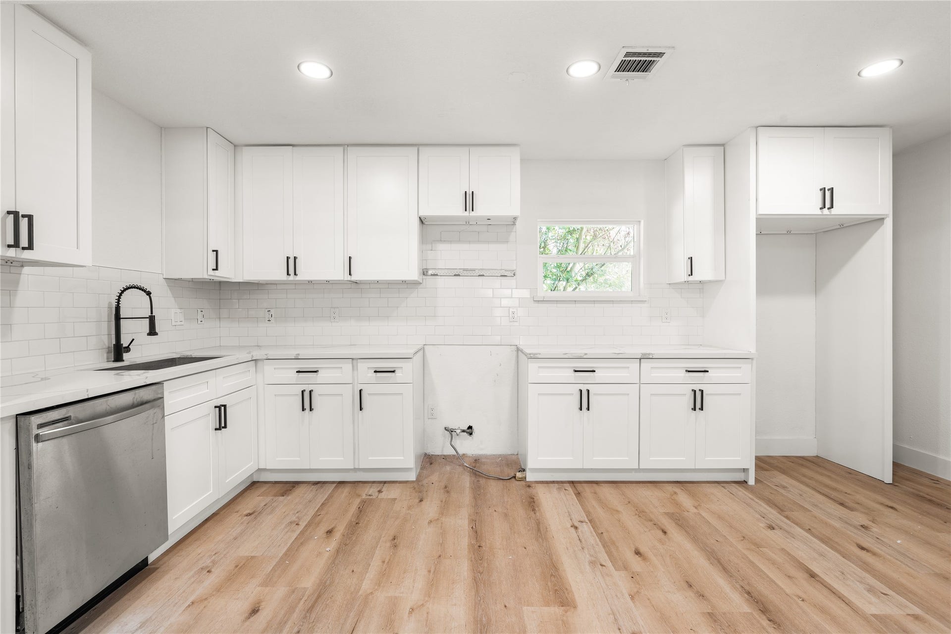 3048 Briarwick Lane, Houston, TX 77093 Modern kitchen showcasing sleek white shaker cabinets, classic subway tile, matte black accents, and rich wood-grain flooring.