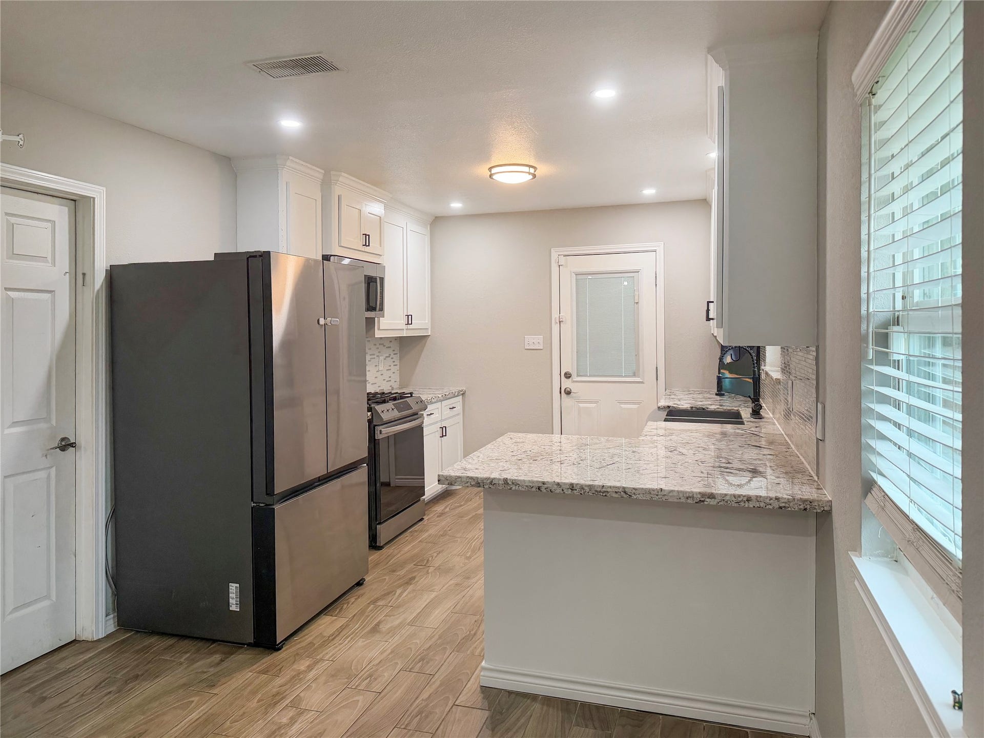 816 W Mulberry, Angleton, TX 77515 Kitchen features white cabinetry, a stainless steel sink, and a window overlooking the backyard, bringing in natural light and offering pleasant outdoor views.
