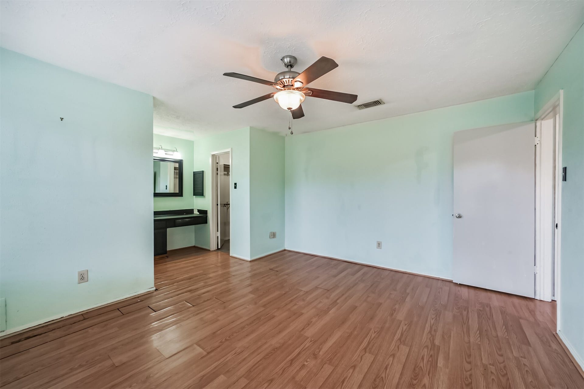 16510 Quiet Quail Drive, Houston, TX 77489 Spacious bedroom featuring laminate flooring, soft mint walls, a ceiling fan, and an attached vanity area for convenience.