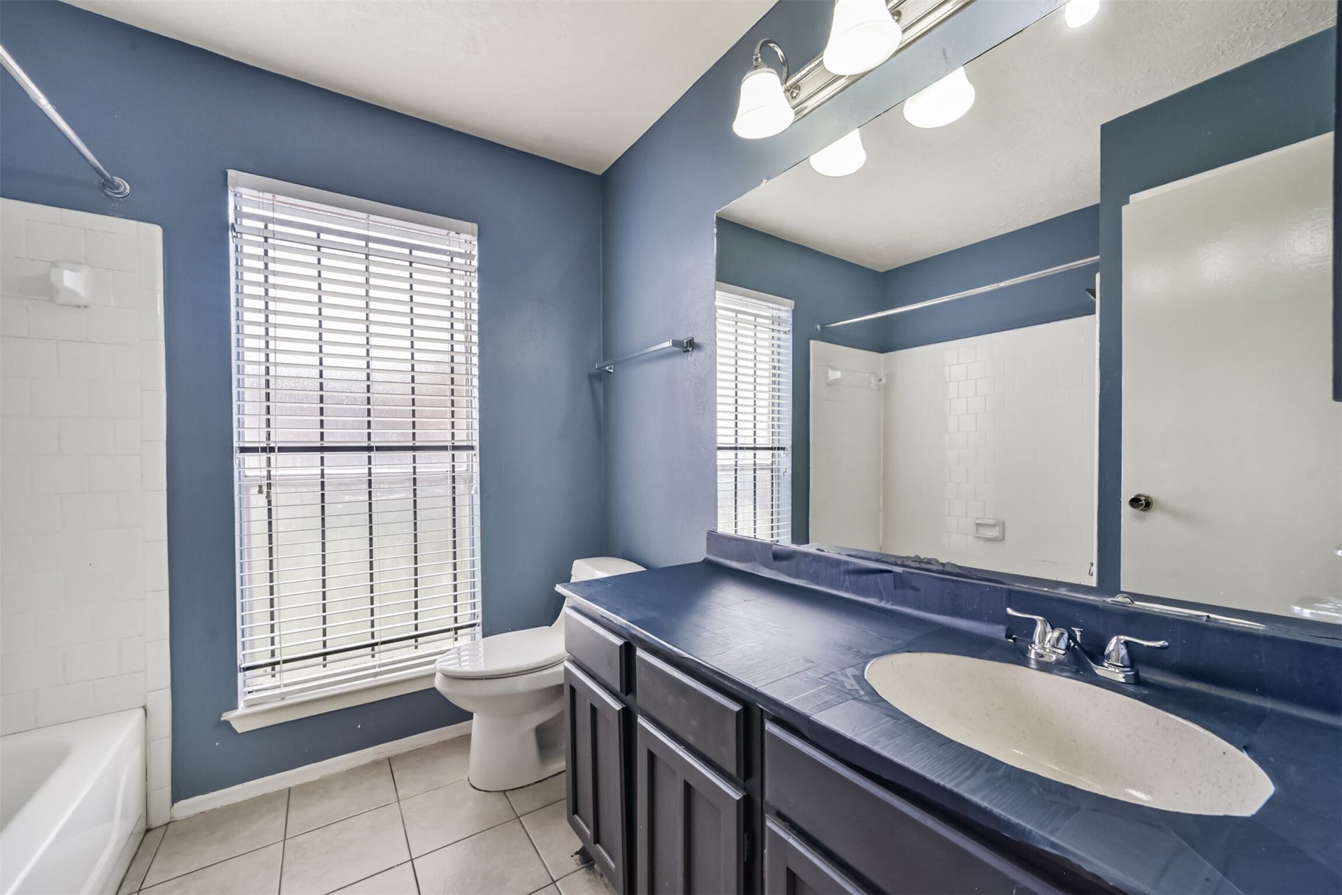 16510 Quiet Quail Drive, Houston, TX 77489 Charming bathroom with a spacious vanity, elegant blue walls, and abundant natural light from a large window, complemented by a classic white tub and modern fixtures.