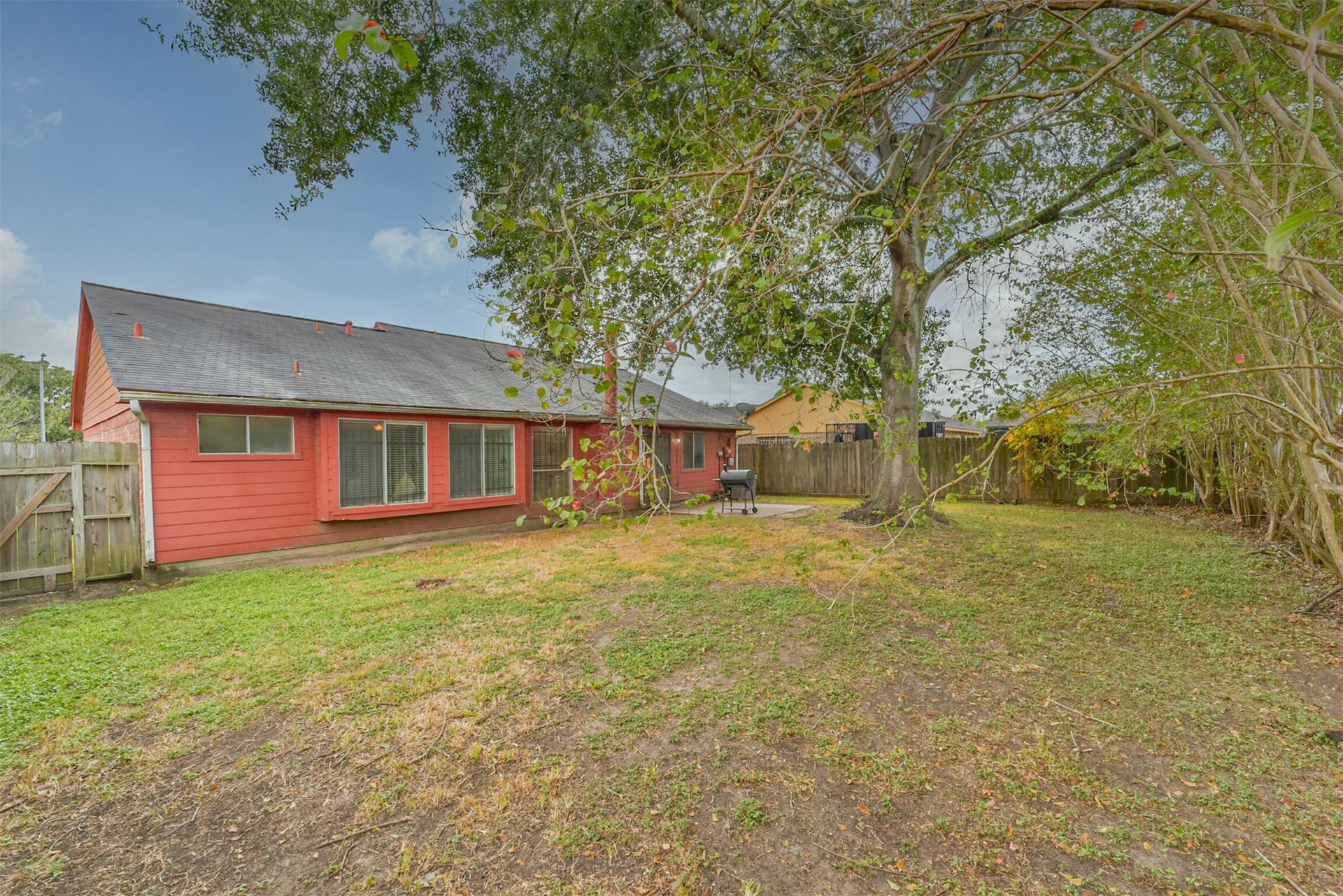 16510 Quiet Quail Drive, Houston, TX 77489 Spacious backyard featuring a charming red house with ample lawn space, mature trees for shade, and a cozy patio area perfect for outdoor gatherings.