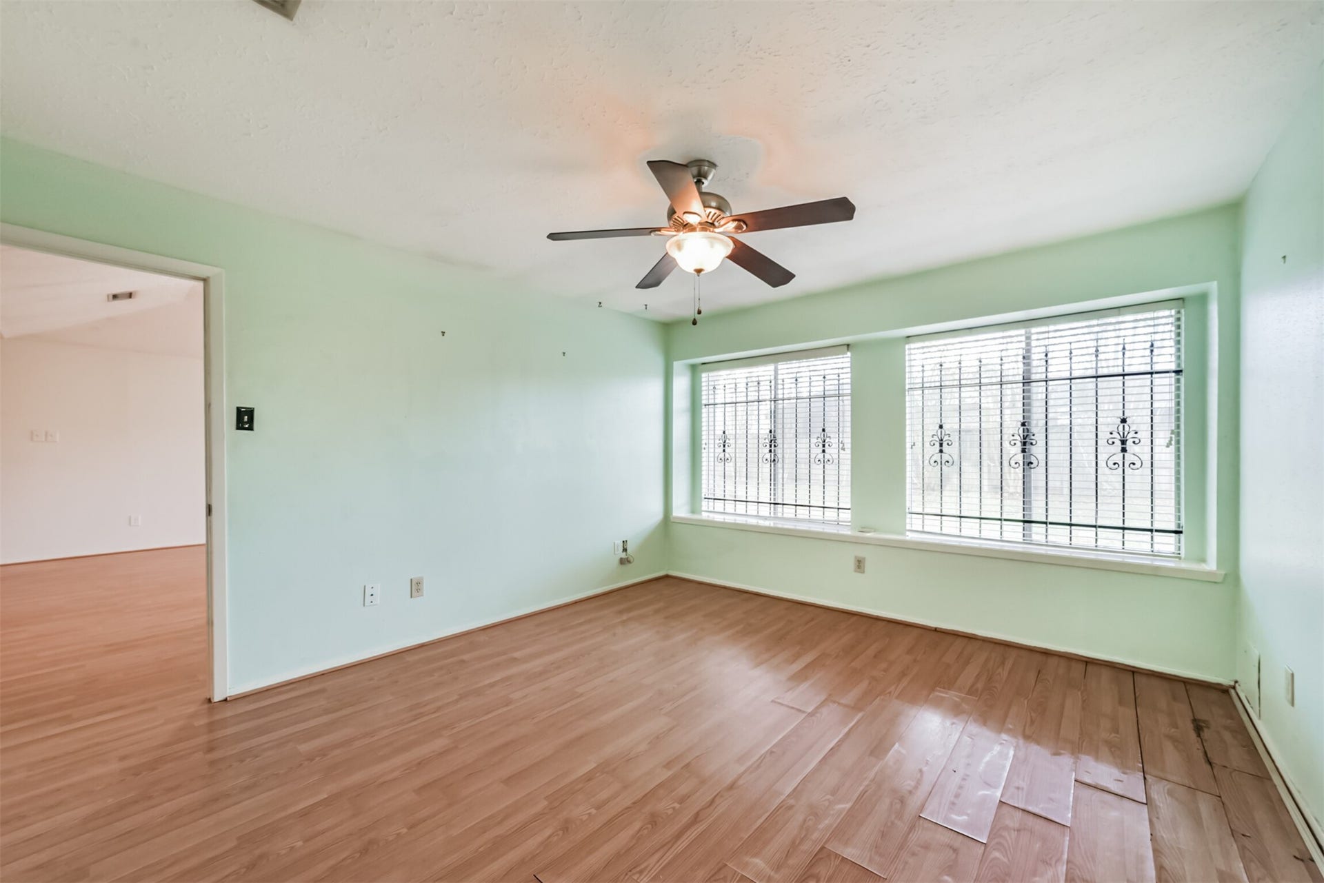 16510 Quiet Quail Drive, Houston, TX 77489 Bright room with large windows featuring decorative ironwork, sleek laminate flooring, and a ceiling fan for added comfort and style.