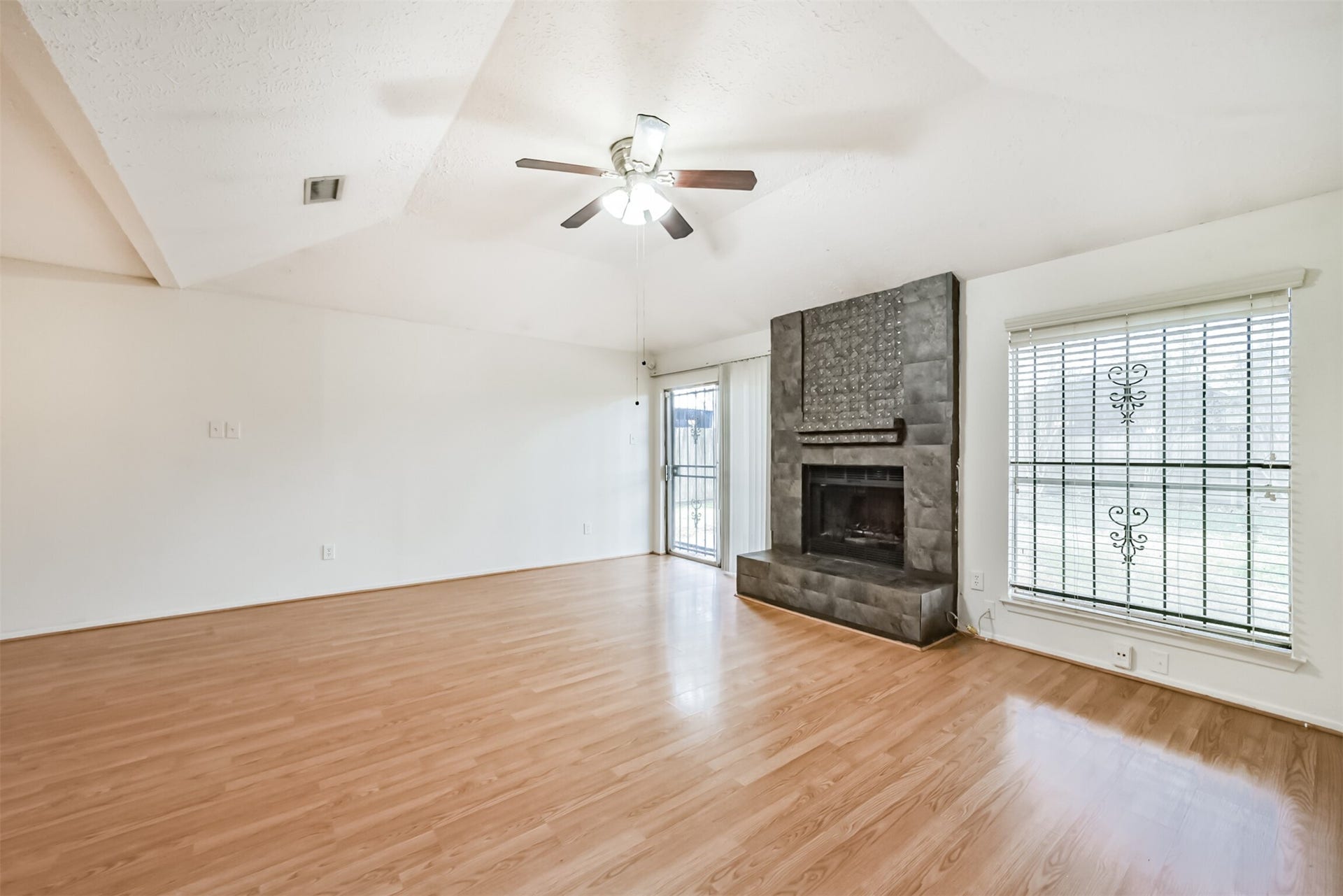16510 Quiet Quail Drive, Houston, TX 77489 Spacious living room featuring elegant wood flooring, a modern ceiling fan, and a striking stone fireplace, accented by large windows for abundant natural light.