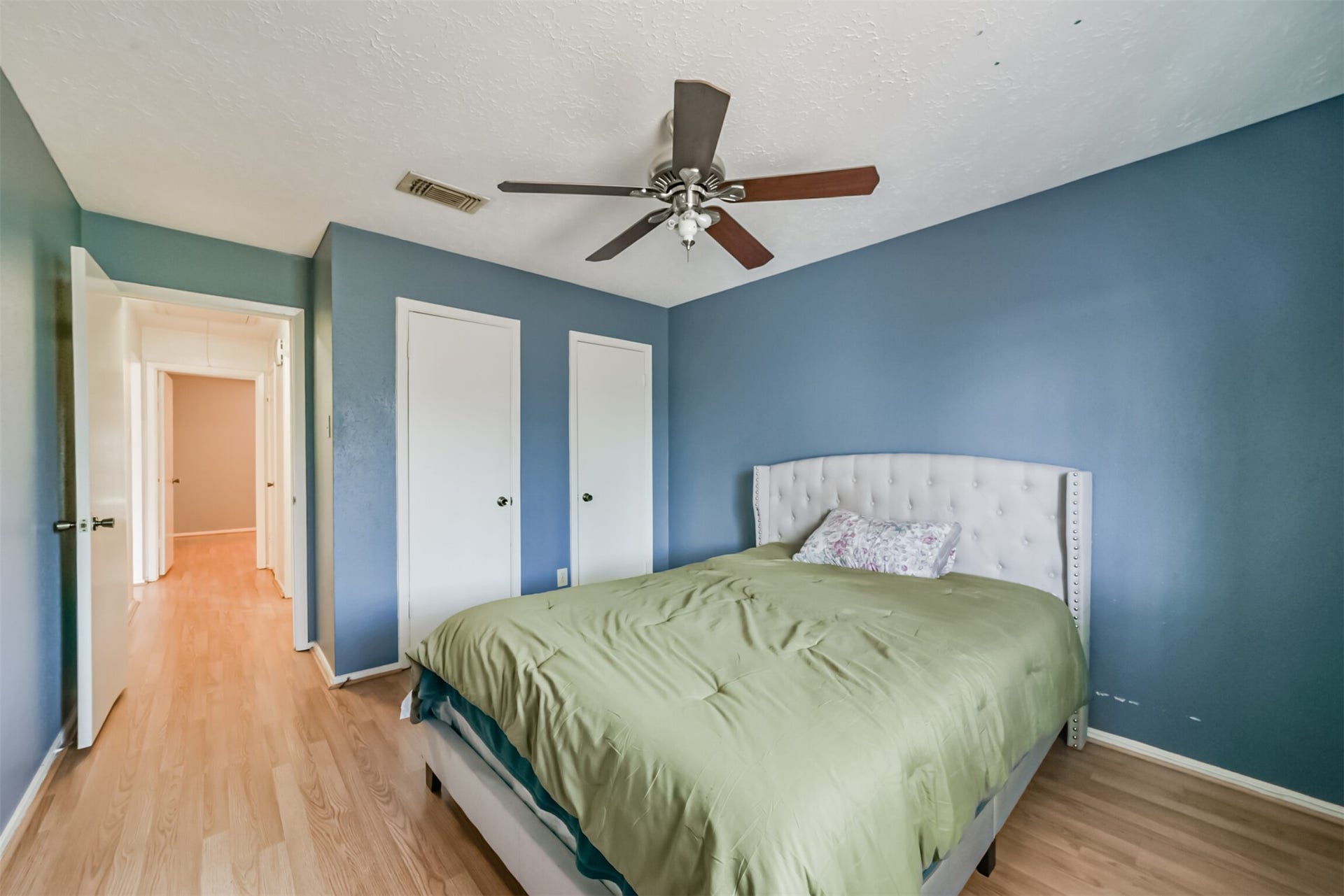 16510 Quiet Quail Drive, Houston, TX 77489 Cozy bedroom featuring a stylish tufted headboard, elegant ceiling fan, and warm wood flooring, accented by serene blue walls.