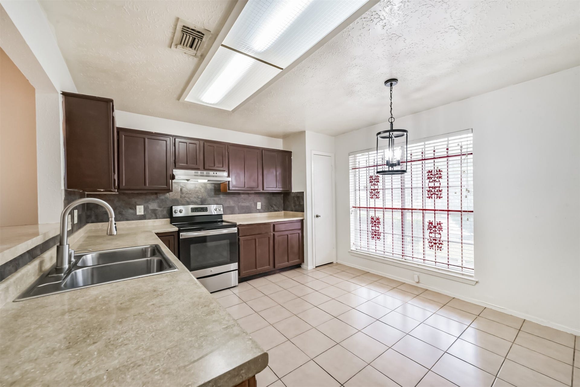 16510 Quiet Quail Drive, Houston, TX 77489 Spacious kitchen with modern stainless steel appliances, rich wooden cabinetry, and ample counter space, complemented by a bright dining area with large windows and elegant tile flooring.