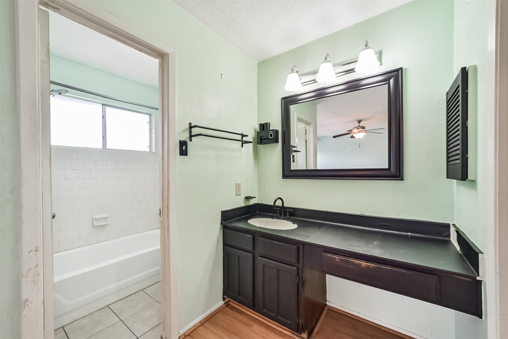 16510 Quiet Quail Drive, Houston, TX 77489 Charming bathroom with a modern black vanity, spacious mirror, and bright lighting, leading to a tiled bathtub area with natural light.