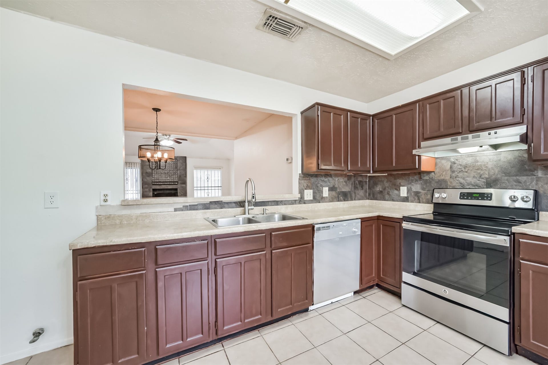 16510 Quiet Quail Drive, Houston, TX 77489 Charming kitchen with rich wood cabinetry, modern stainless steel appliances, and a convenient pass-through window to the cozy living area featuring a fireplace.