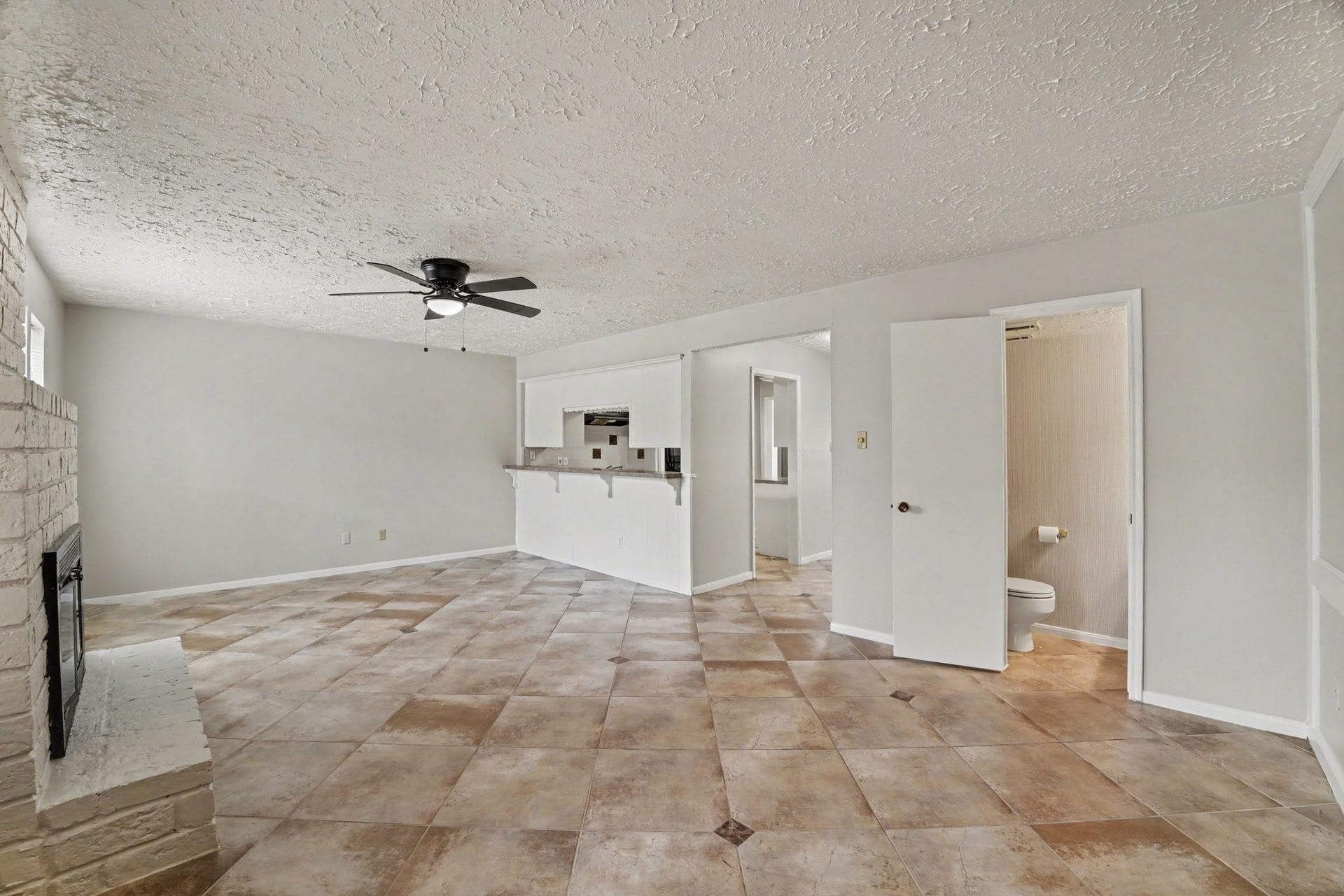 44 Chapparal Court, Missouri City, TX 77459 A long breakfast bar counter with an integrated pass-through to the kitchen makes serving and entertaining effortless while maintaining open sightlines across the home. Overhead, a contemporary black ceiling fan provides comfort, and the room is anchored by durable, oversized diagonal tile flooring that stretches across the bright, light-filled layout.