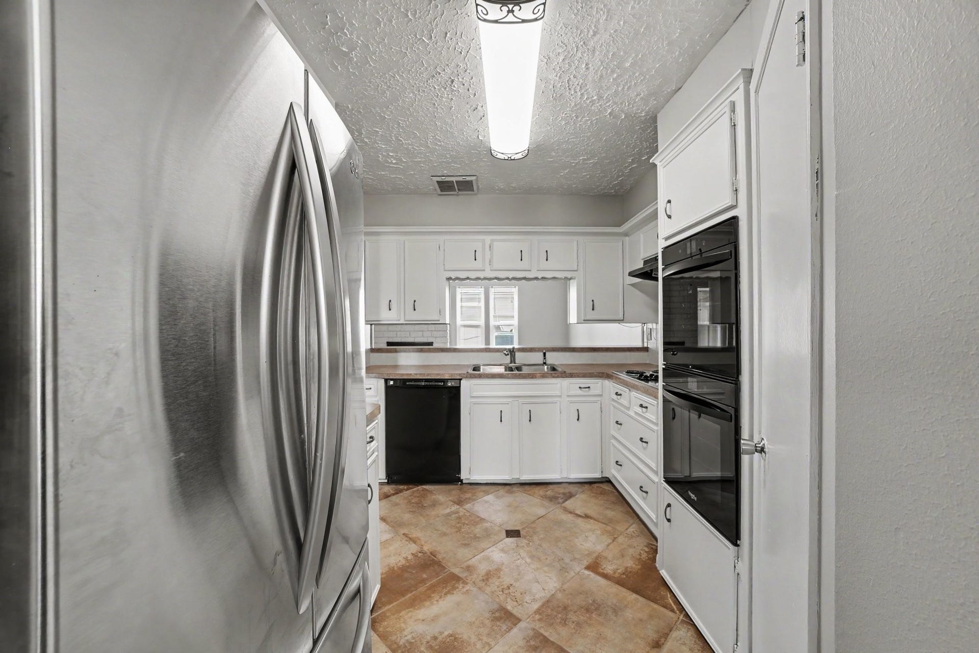 44 Chapparal Court, Missouri City, TX 77459 The bright and functional kitchen boasts classic white cabinetry paired with dark and stainless-steel appliances, including a double wall oven, a sleek black dishwasher, and a spacious stainless-steel refrigerator.