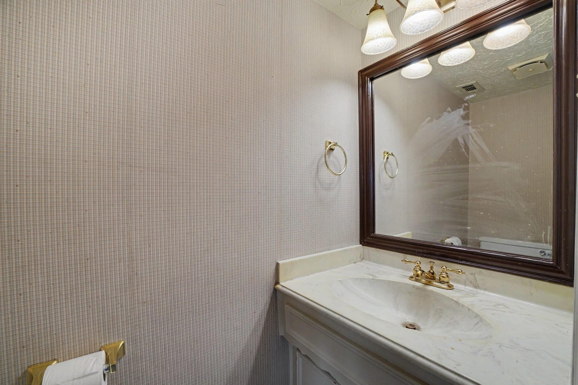 44 Chapparal Court, Missouri City, TX 77459 Conveniently located on the main floor, this half-bath powder room blends classic design elements with everyday utility. Textured, neutral grasscloth-style wallpaper adds warm visual depth to the walls, complemented by elegant brass fixtures including a towel ring, toilet paper holder, and a sleek brass faucet.