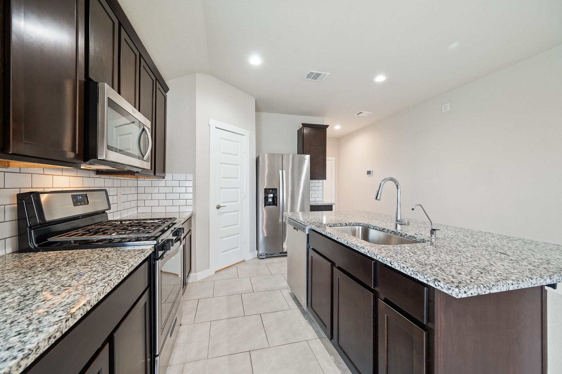 This inviting kitchen features tile flooring, tile backsplash, dark wood cabinetry and a large island with seating.