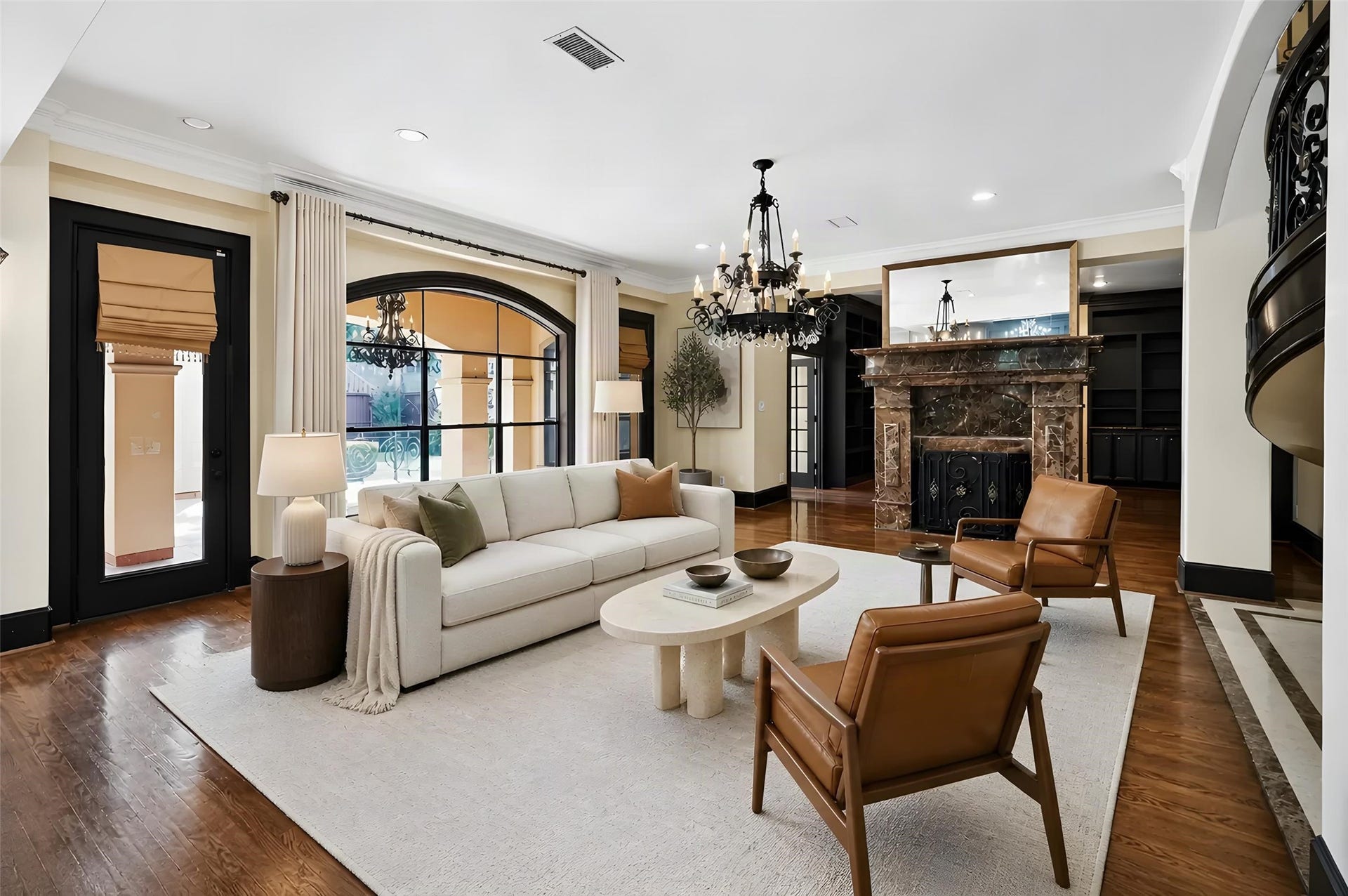 Elegant living room featuring a grand marble fireplace, rich hardwood floors, and abundant natural light through large arched windows. *Photo is virtually staged*