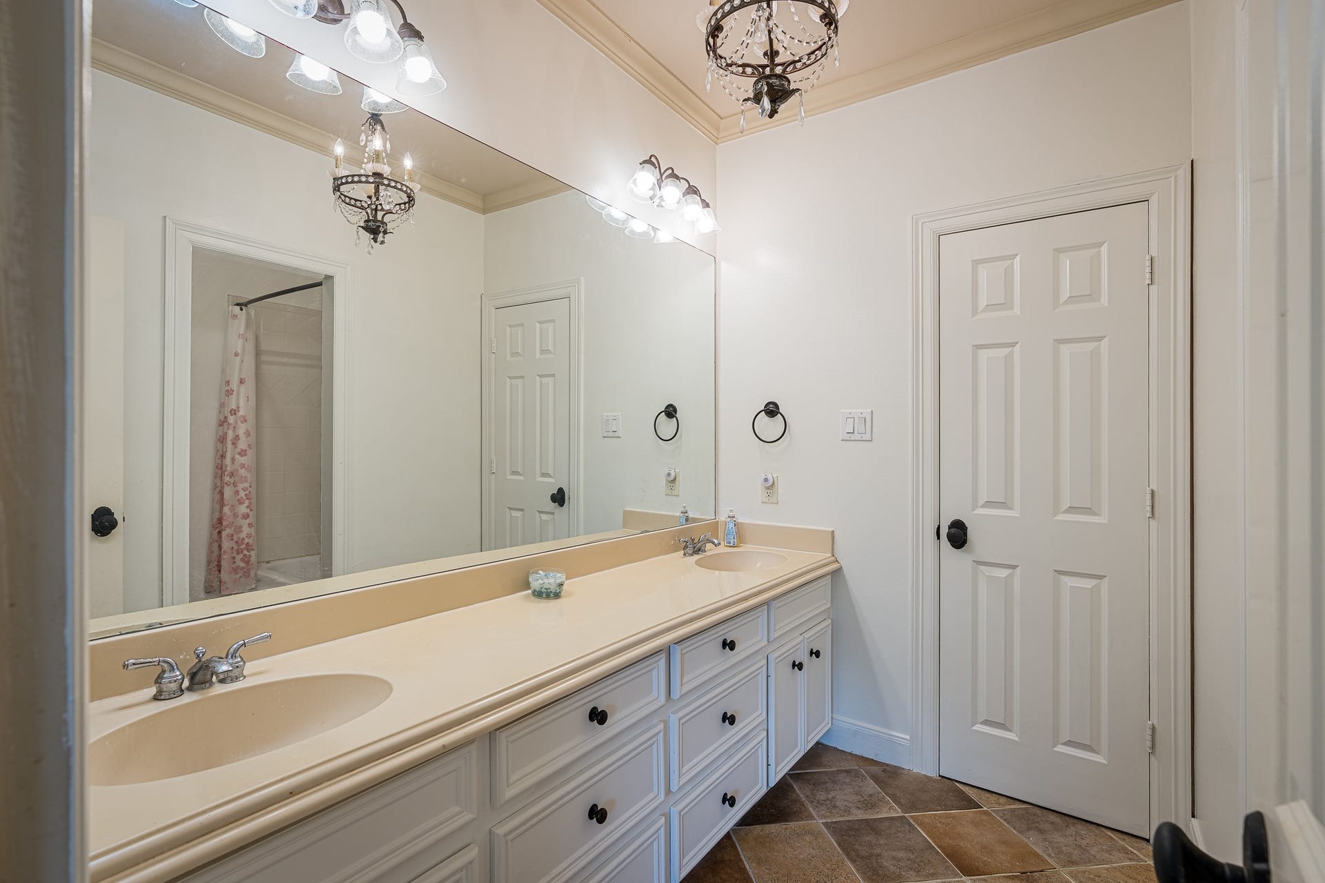 Elegant bathroom featuring a spacious double vanity with ample storage, stylish lighting fixtures, and a chic tile floor, offering both functionality and charm.