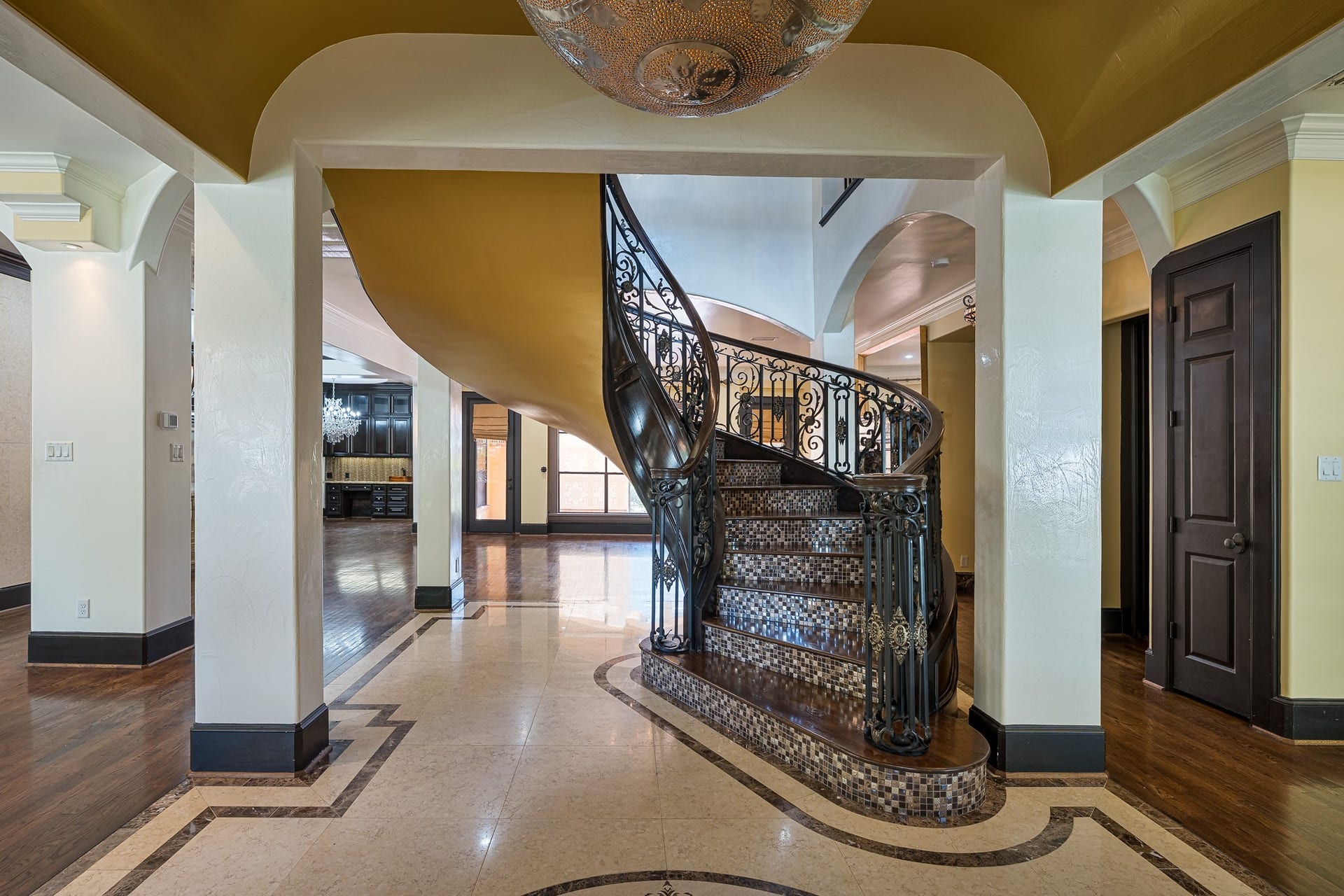 Elegant foyer featuring a stunning spiral staircase with intricate wrought-iron railings, complemented by rich solid-wood and tile accents.