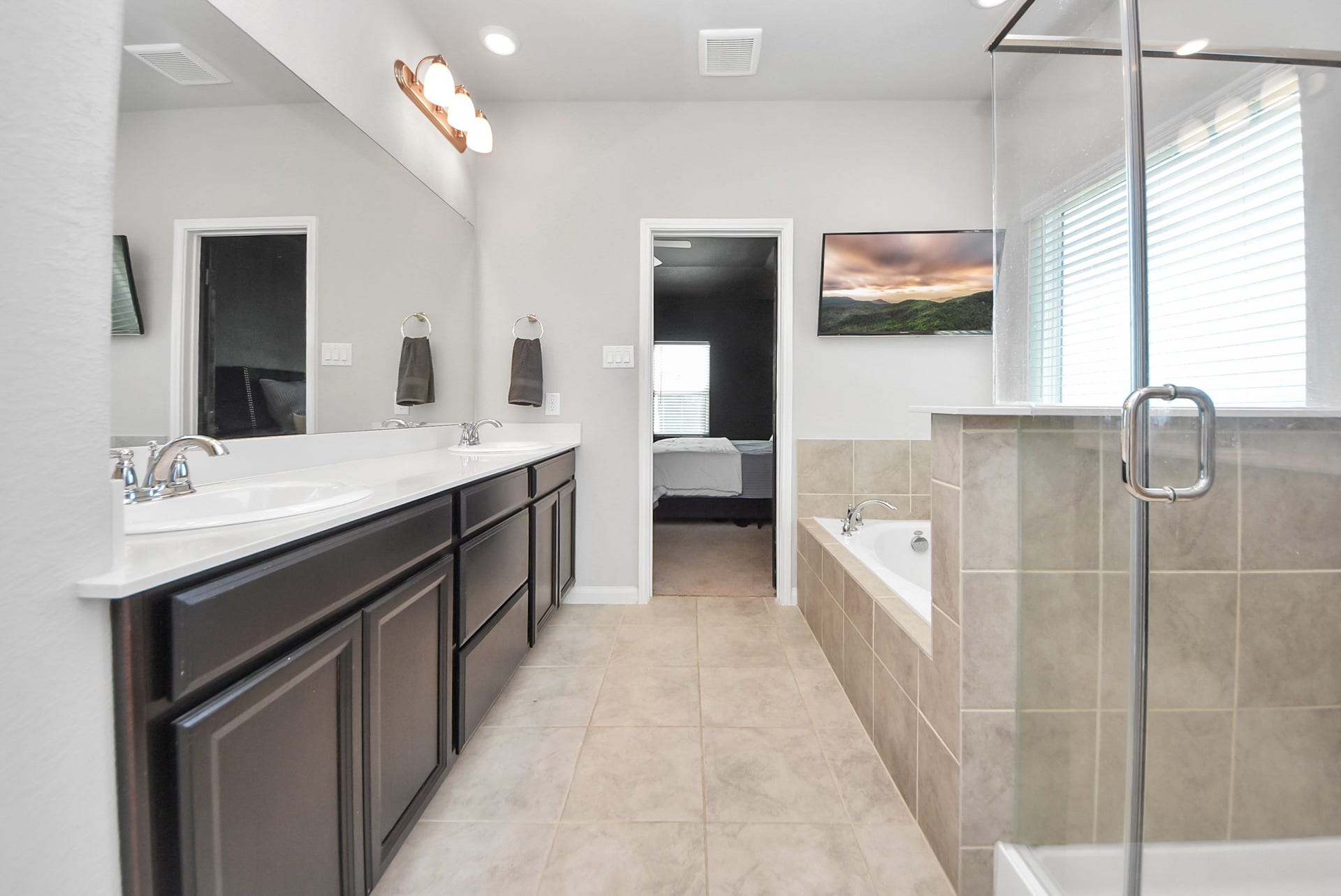 930 Pismo Lane, Rosharon, TX 77583 This is a spacious and modern bathroom featuring a double vanity with cabinets, a glass-enclosed shower, and a separate soaking bathtub. The room is brightened by large window and modern lighting, offering a clean and relaxing atmosphere.