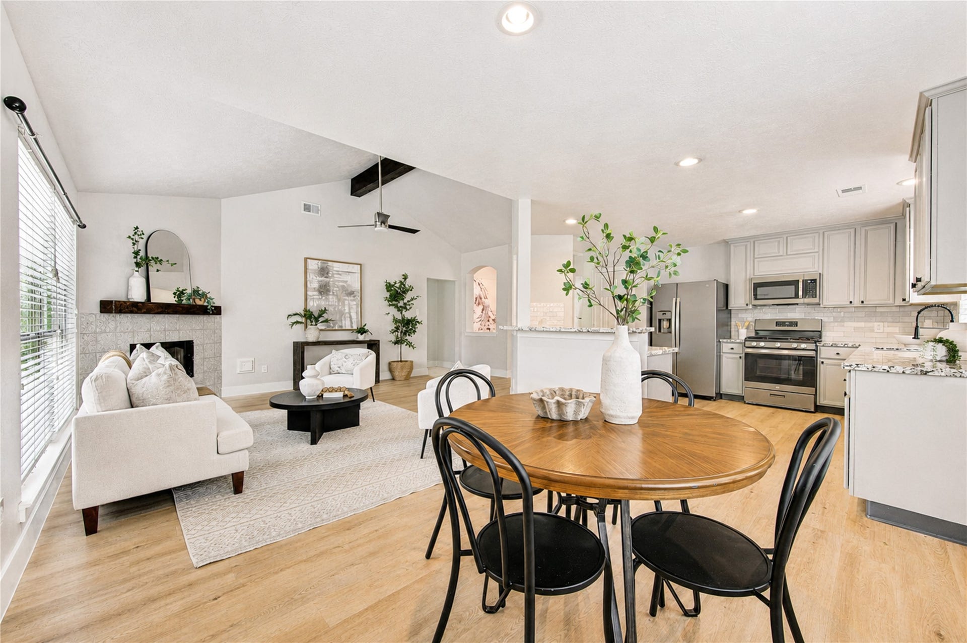 4931 Lake Catherine Court, Richmond, TX 77407 living room featuring a dramatic vaulted ceiling, rich wood beam, statement fireplace and polished sightlines into the kitchen