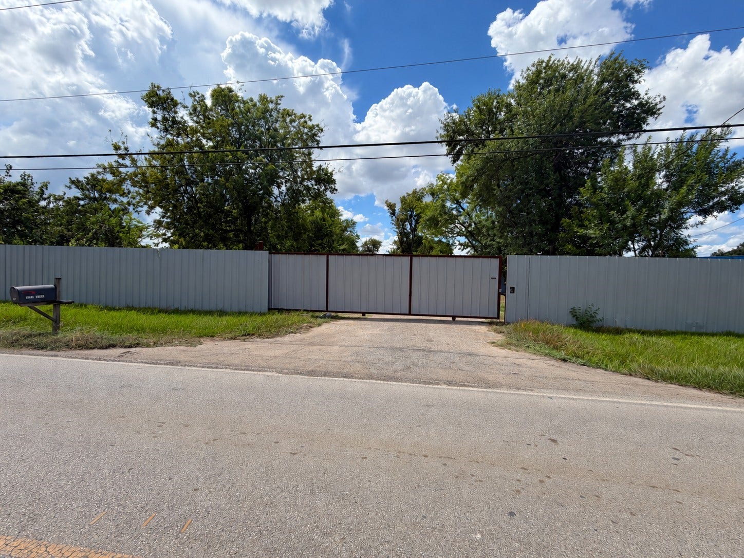 Private gated entrance framed by a full privacy fence, set back from the road on nearly an acre of commercial/residential-zoned land.