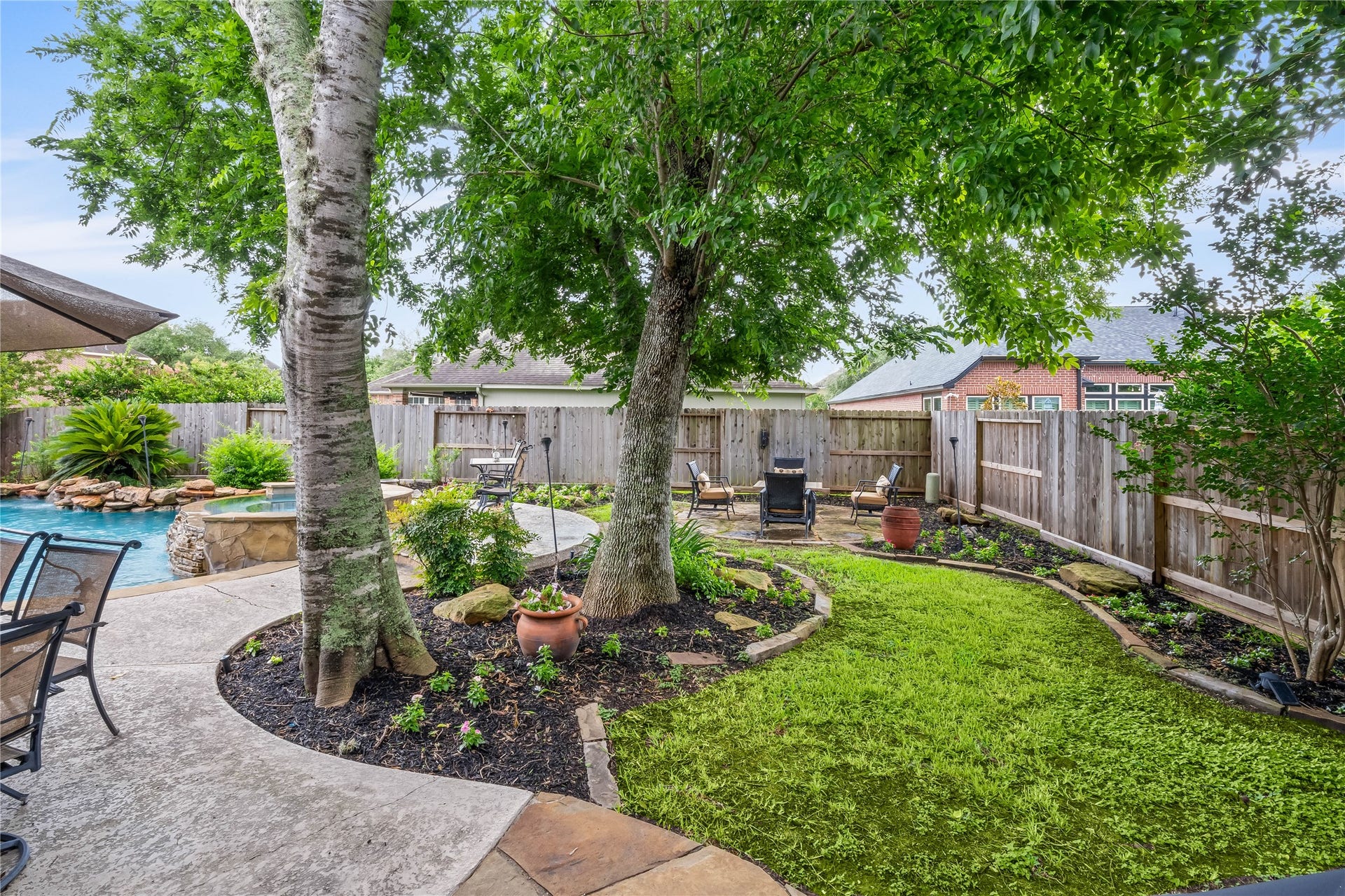 7914 Chianti Court, Sugar Land, TX 77479 Additional backyard space with mature trees, landscaped beds, and seating area offers a peaceful setting for outdoor enjoyment.