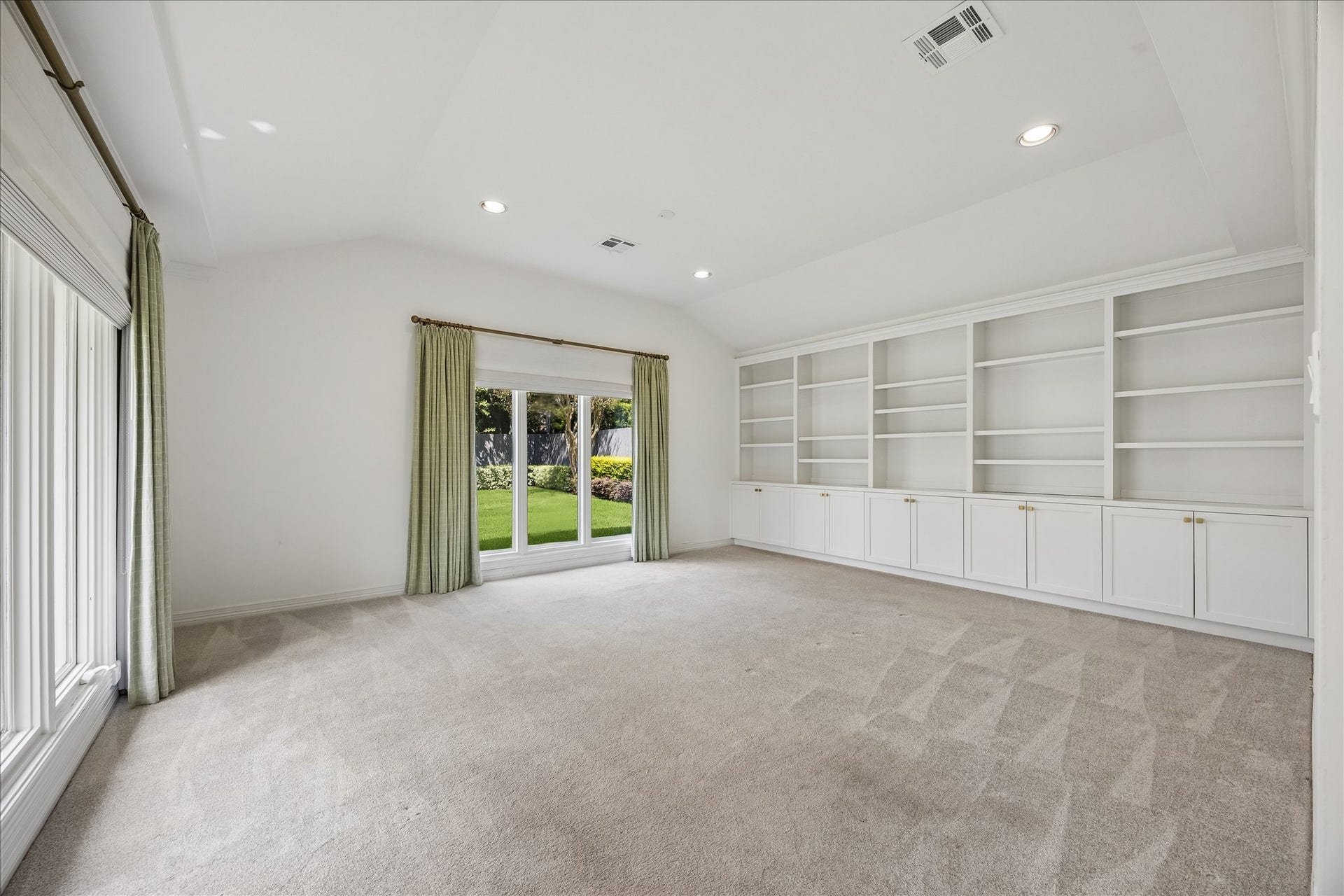 Double doors create an impressive entrance to the light-filled primary suite, featuring a vaulted ceiling, wall of custom built-ins and oversized windows overlooking the backyard. An en suite bath and two generously sized walk-in closets complete the suite.