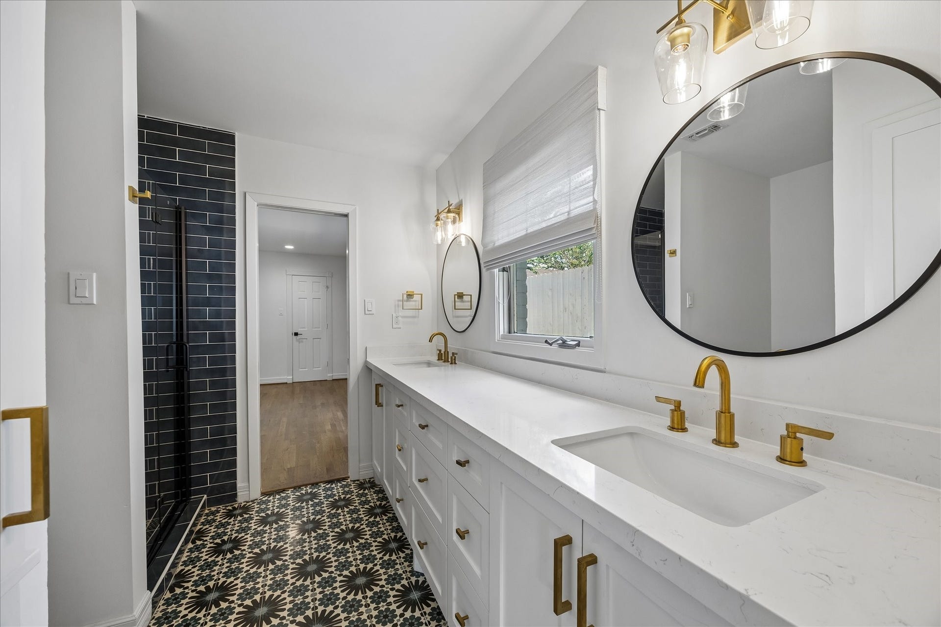 Jack-and-Jill bath features a double vanity with quartz countertops and brass fixtures, a black subway tile shower and decorative patterned tile flooring.