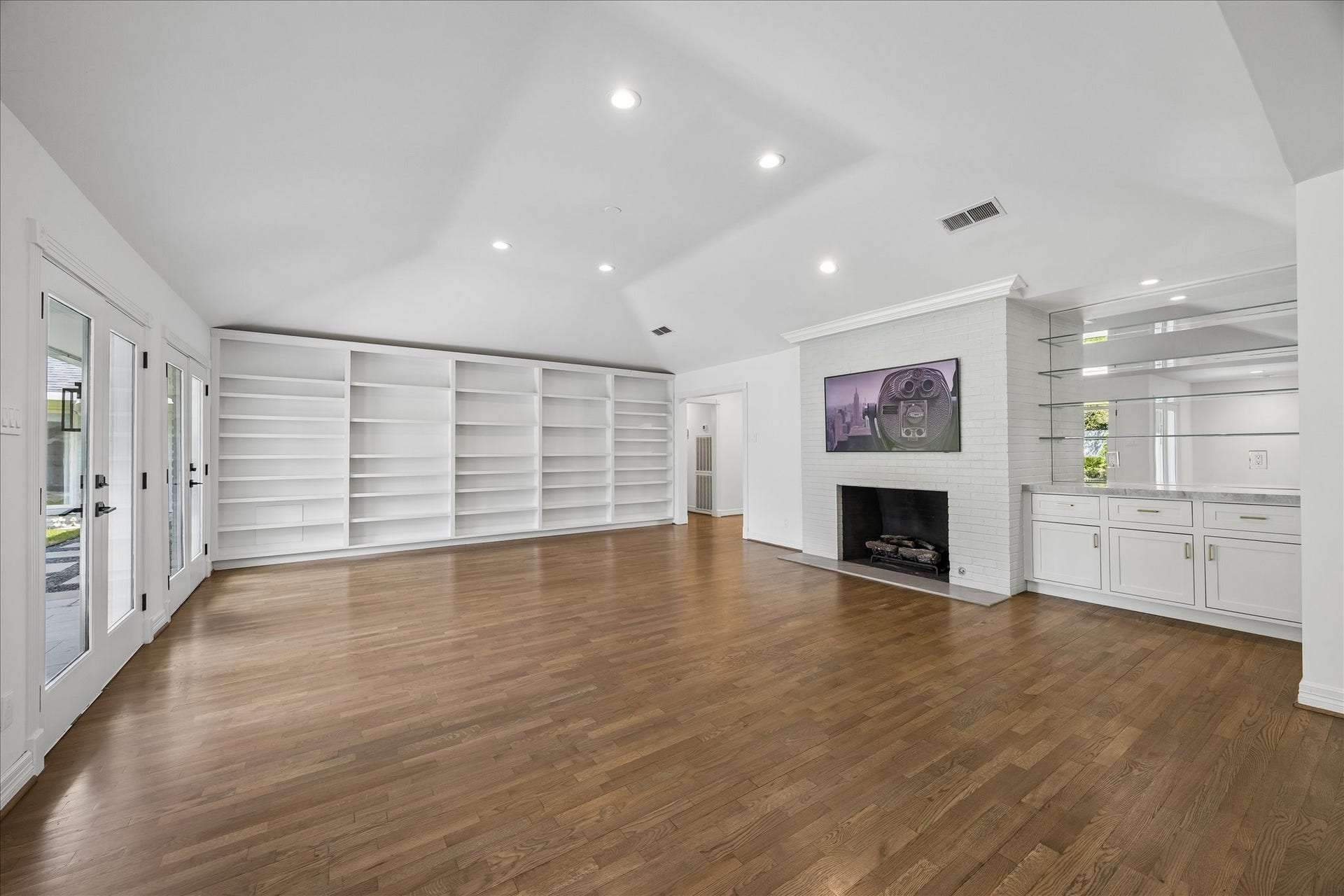 Alternate view of the family room showing expansive custom built-ins, the gas log fireplace and a stylish dry bar with glass shelving and storage.