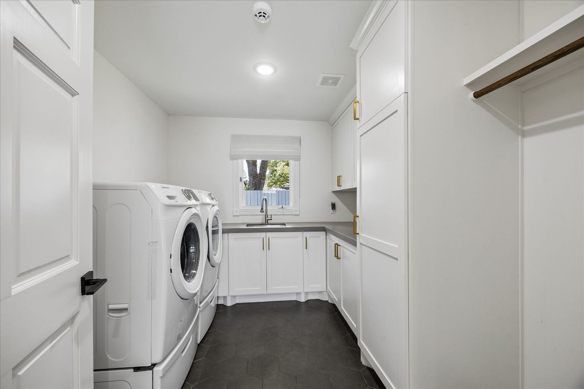 Spacious utility room features quartz countertops, a stainless steel sink, hexagon tile flooring and generous built-in storage.
