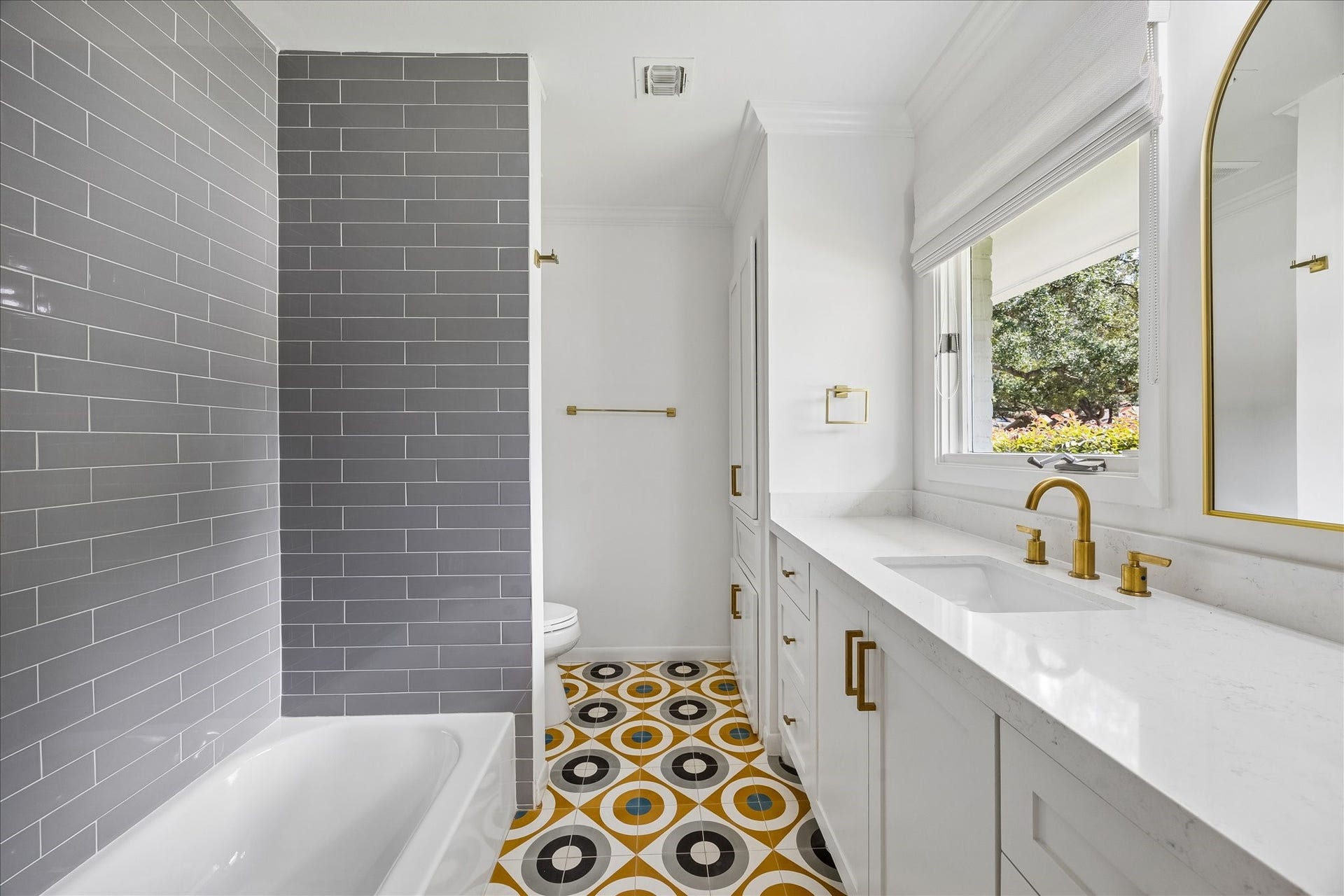 Bright and stylish en-suite bathroom featuring a modern gray subway tile shower, vibrant geometric floor tiles, and elegant gold fixtures.