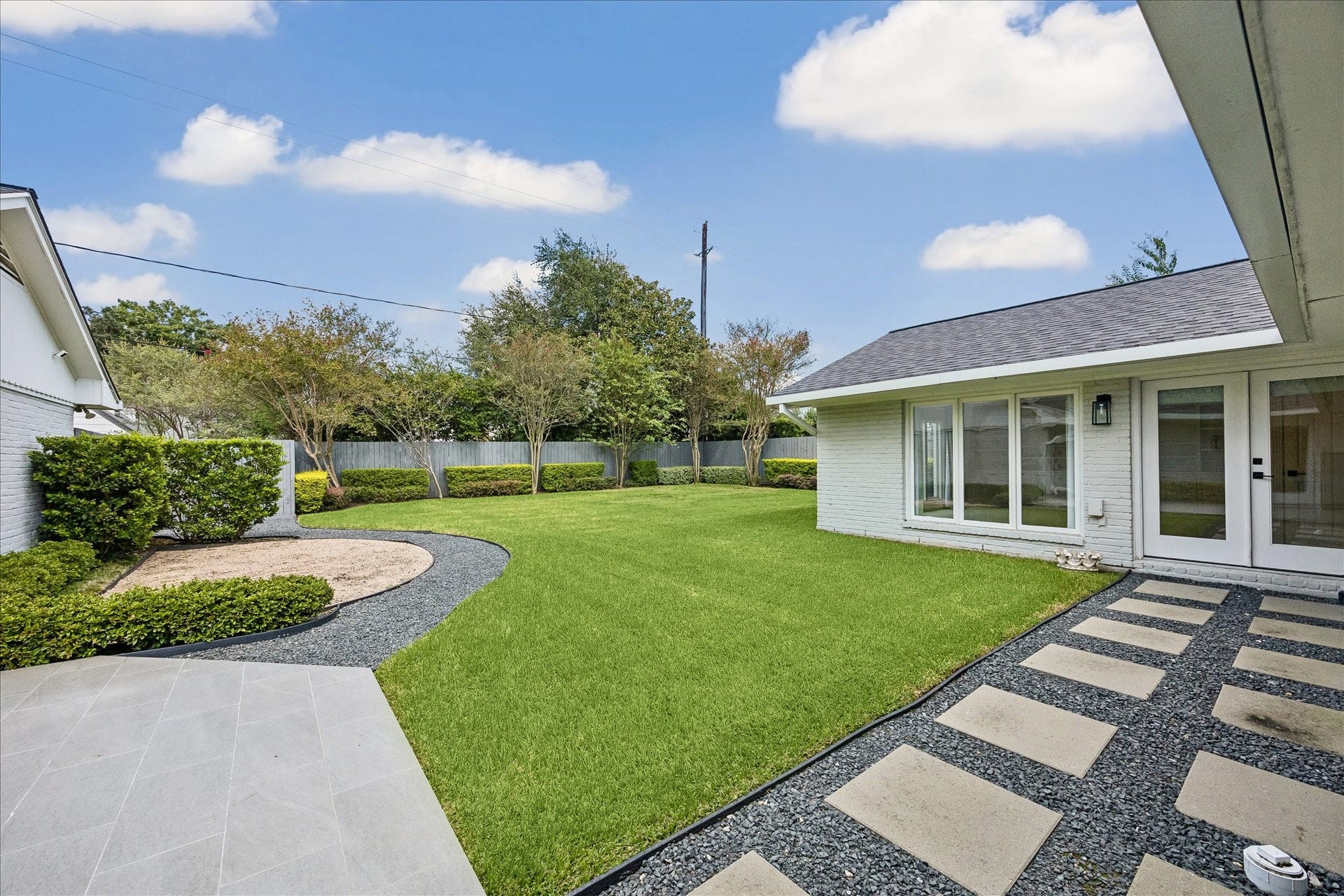 View from the patio highlights the expansive lawn and beautifully manicured backyard, accented by concrete pavers and Black Star gravel.
