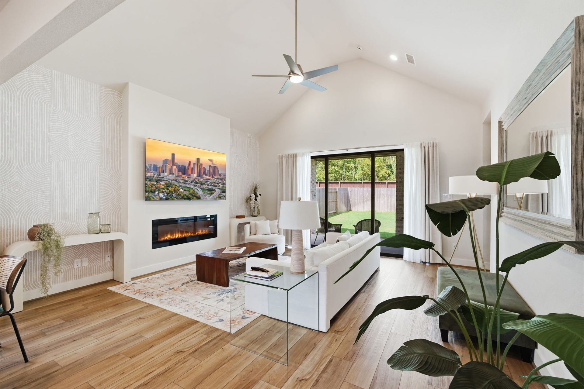 24615 Lukes Landing Way, Tomball, TX 77375 Spacious living room with vaulted ceilings, modern fireplace, and large glass doors leading to a lush backyard. Natural light floods the space, highlighting the elegant decor and hardwood floors.