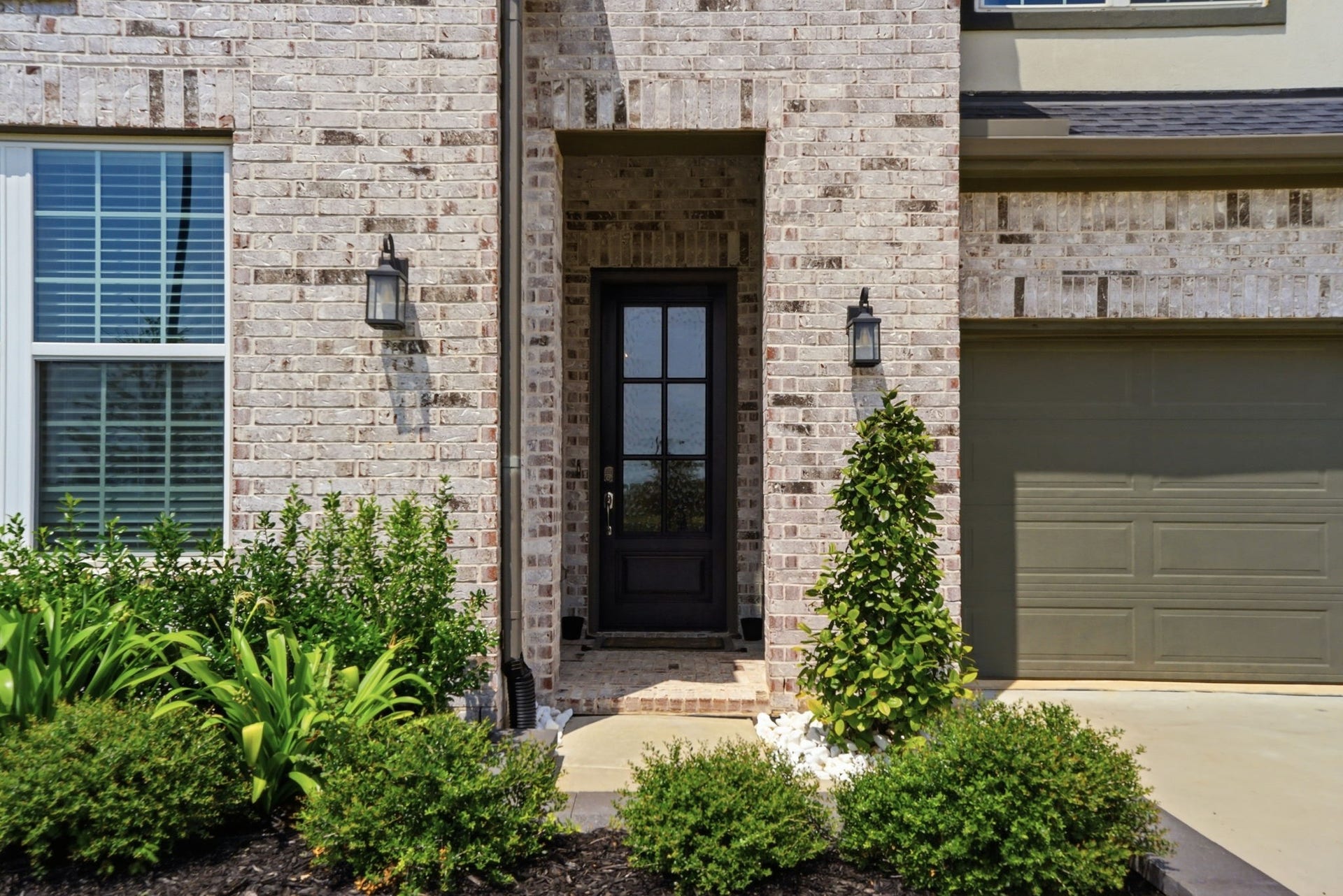24615 Lukes Landing Way, Tomball, TX 77375 Charming brick entryway with elegant lantern lighting, lush greenery, and a classic black door, offering a warm welcome to your new home.