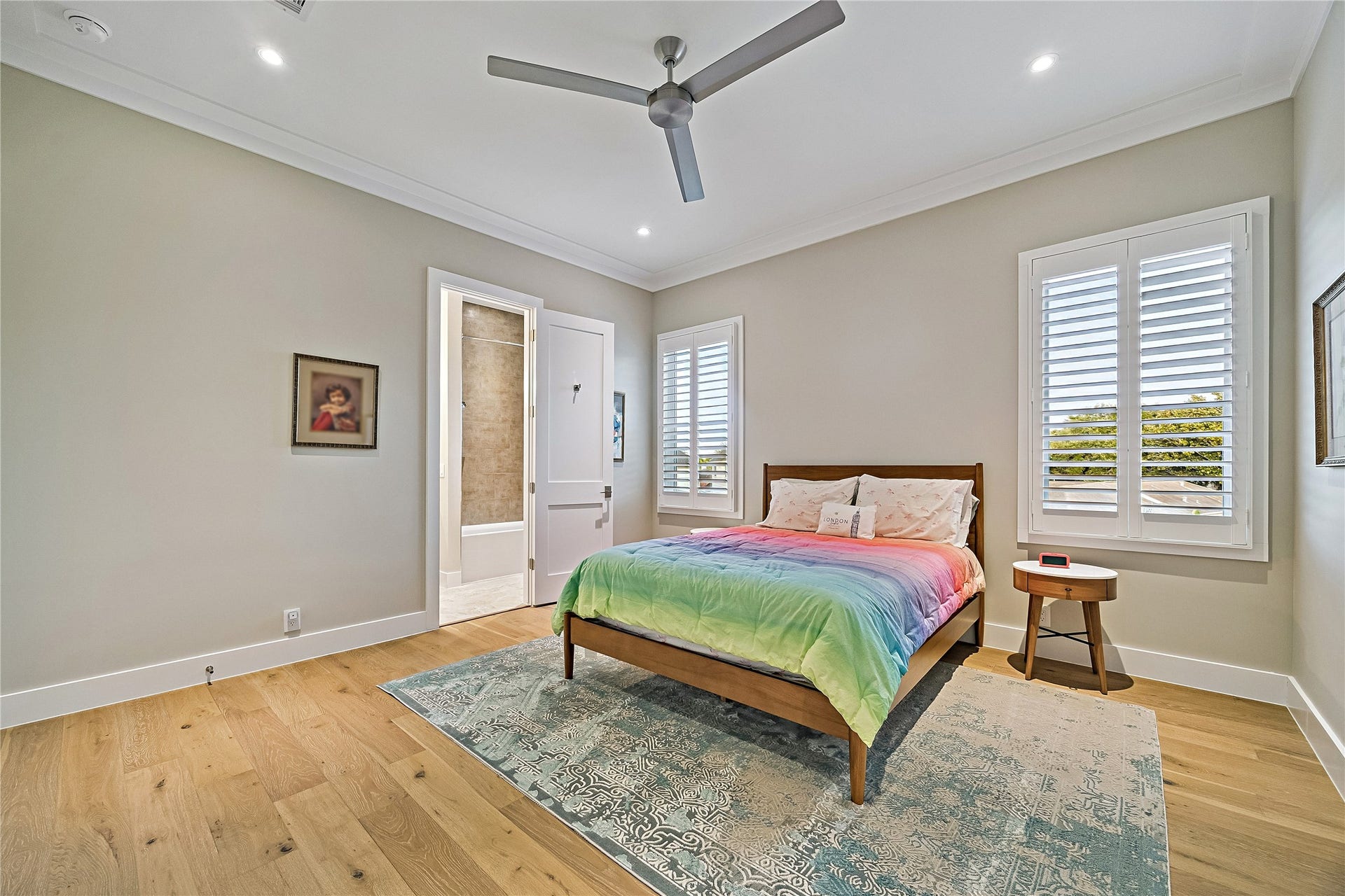 Spacious upper-level bedroom featuring beautiful wood flooring, a ceiling fan, recessed lighting, and multiple windows providing natural light. A comfortable and versatile space for family or guests.