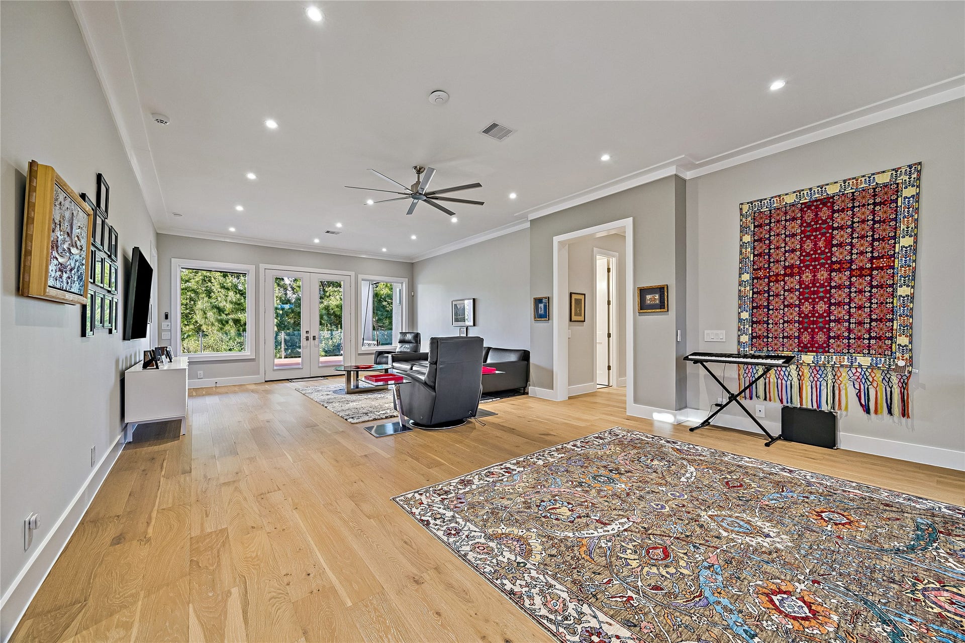 An expansive recreational space featuring beautiful wood flooring, generous seating areas, and multiple windows overlooking the landscape. Direct balcony access connects the room to the home's elevated outdoor living areas.